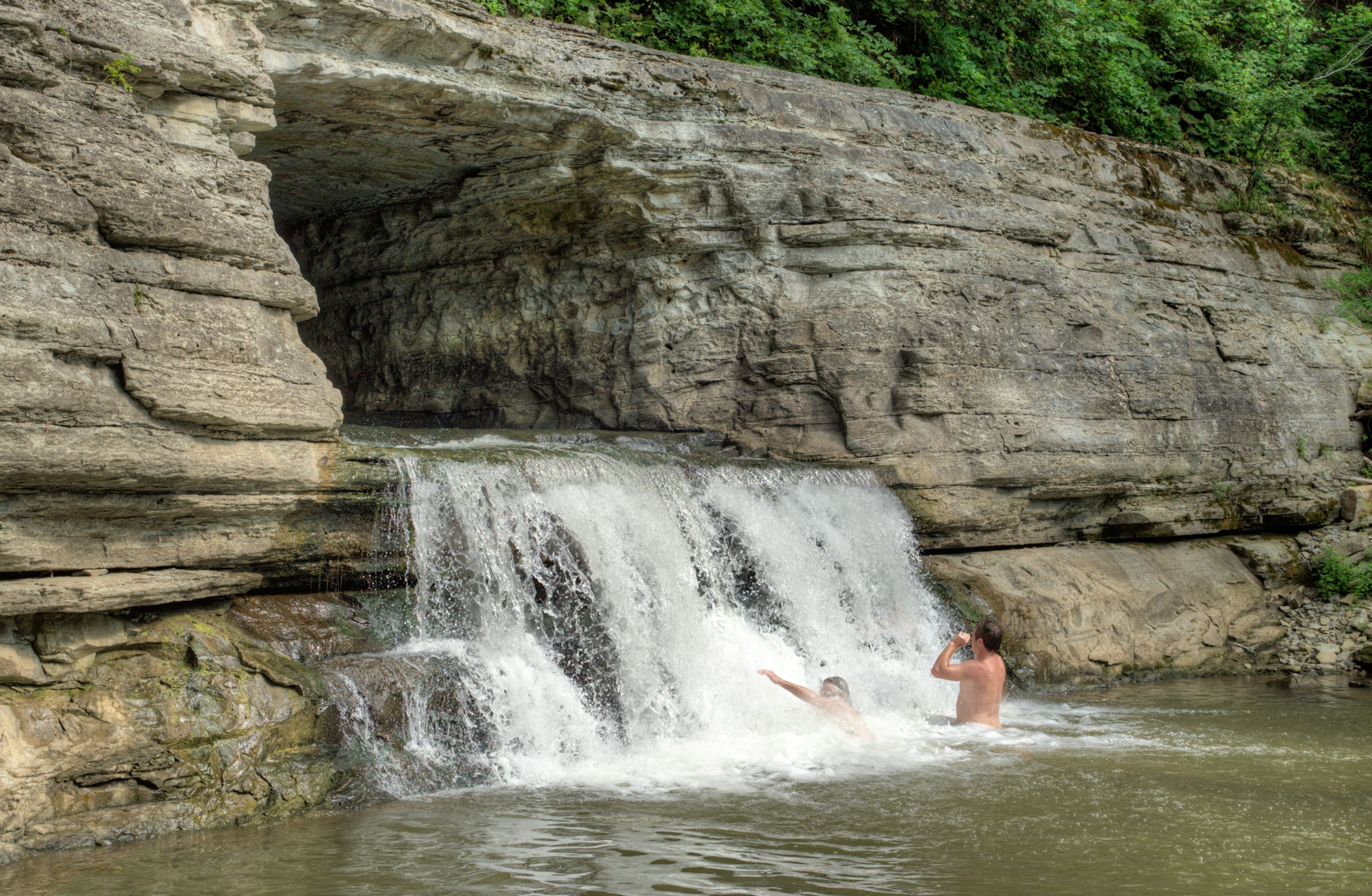 Two people splash in the force of an fast-flowing waterfall