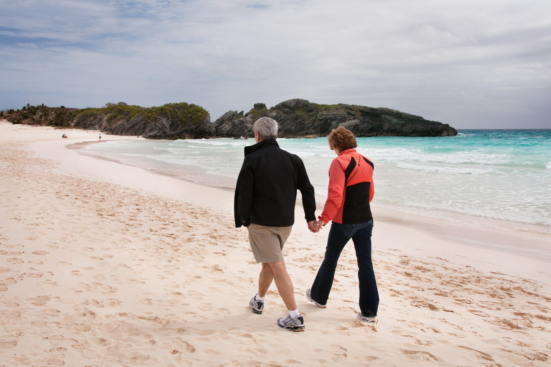 Healthy and fit couple in their 60's, walking on sandy beach in Bermuda in March, holding hands.