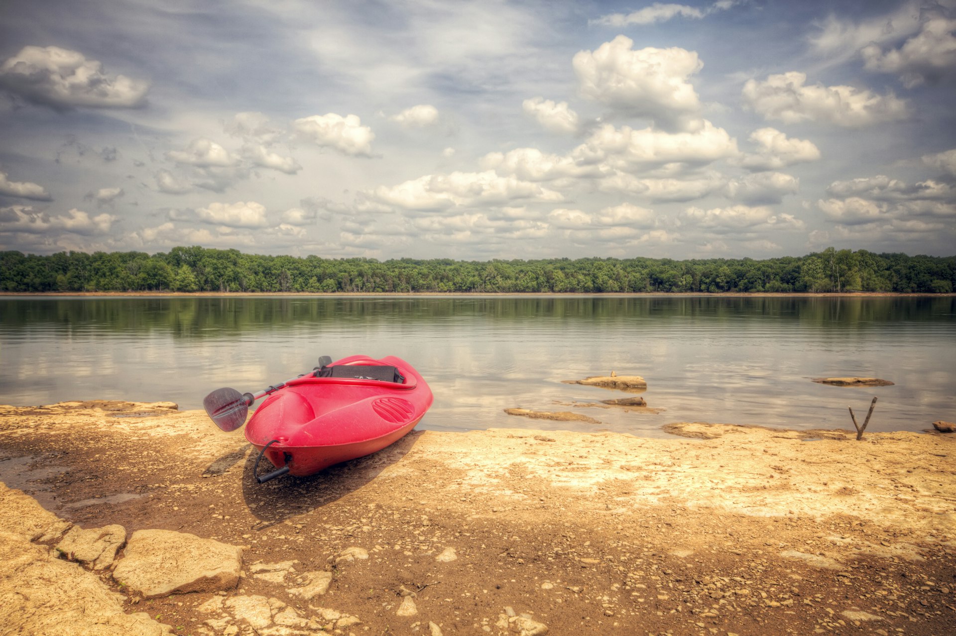 A red kayak sits a the side of a lake on a sunny day