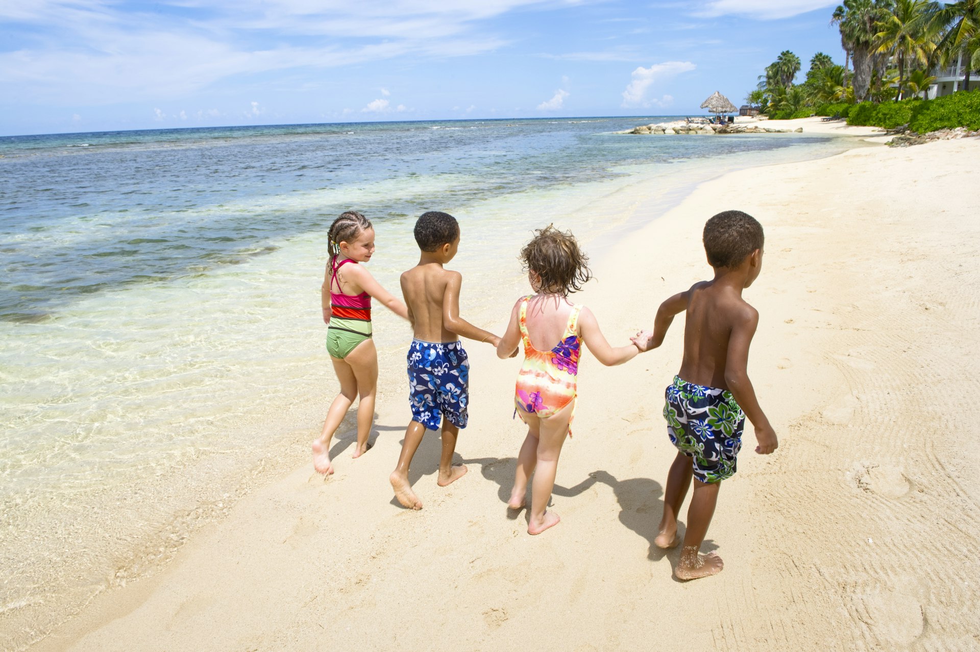 Four young children hold hands as they walk along a sandy beach together