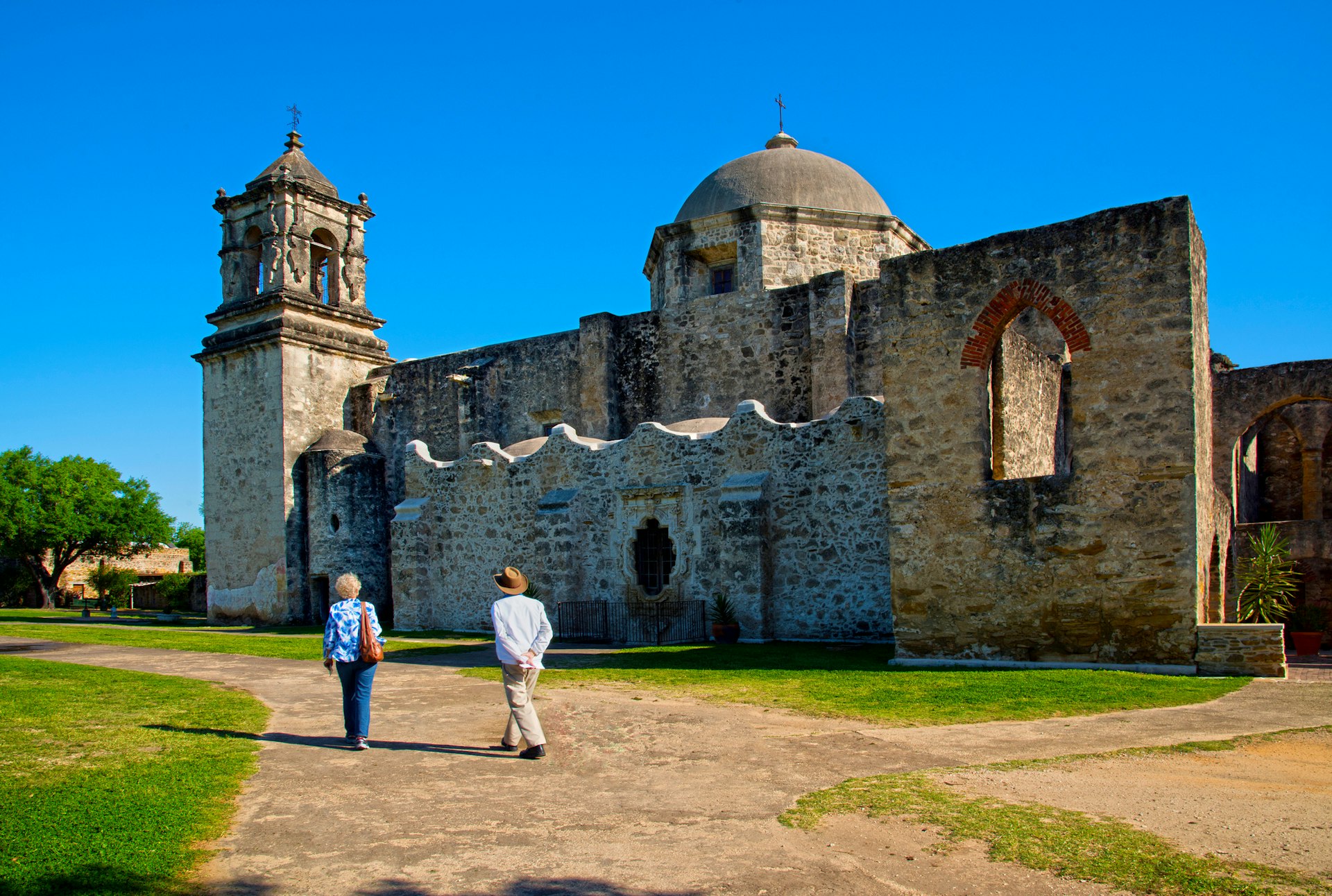 Two people walk in the grounds of a historic Mission building