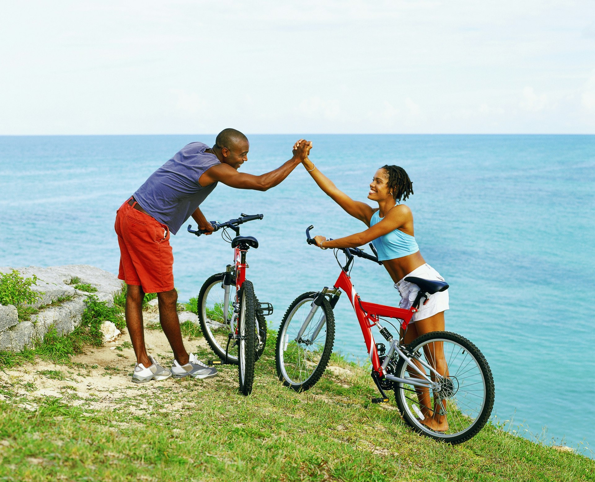 A couple celebrate cycling to the top of a green hill overlooking the sea in Bermuda
