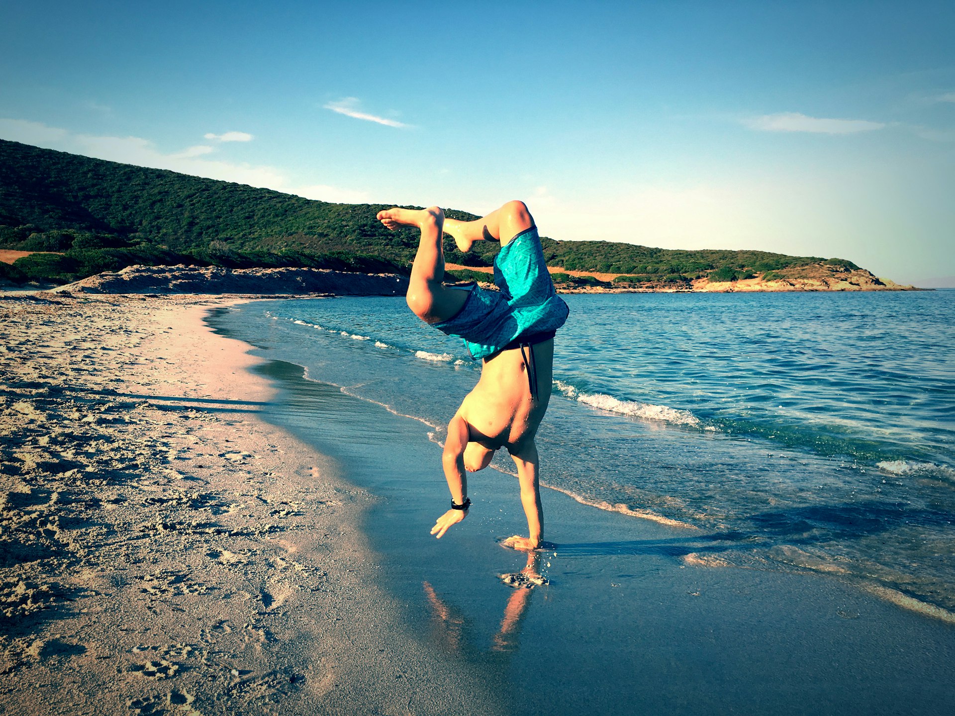 A young boy does a handstand on the beach in Corsica