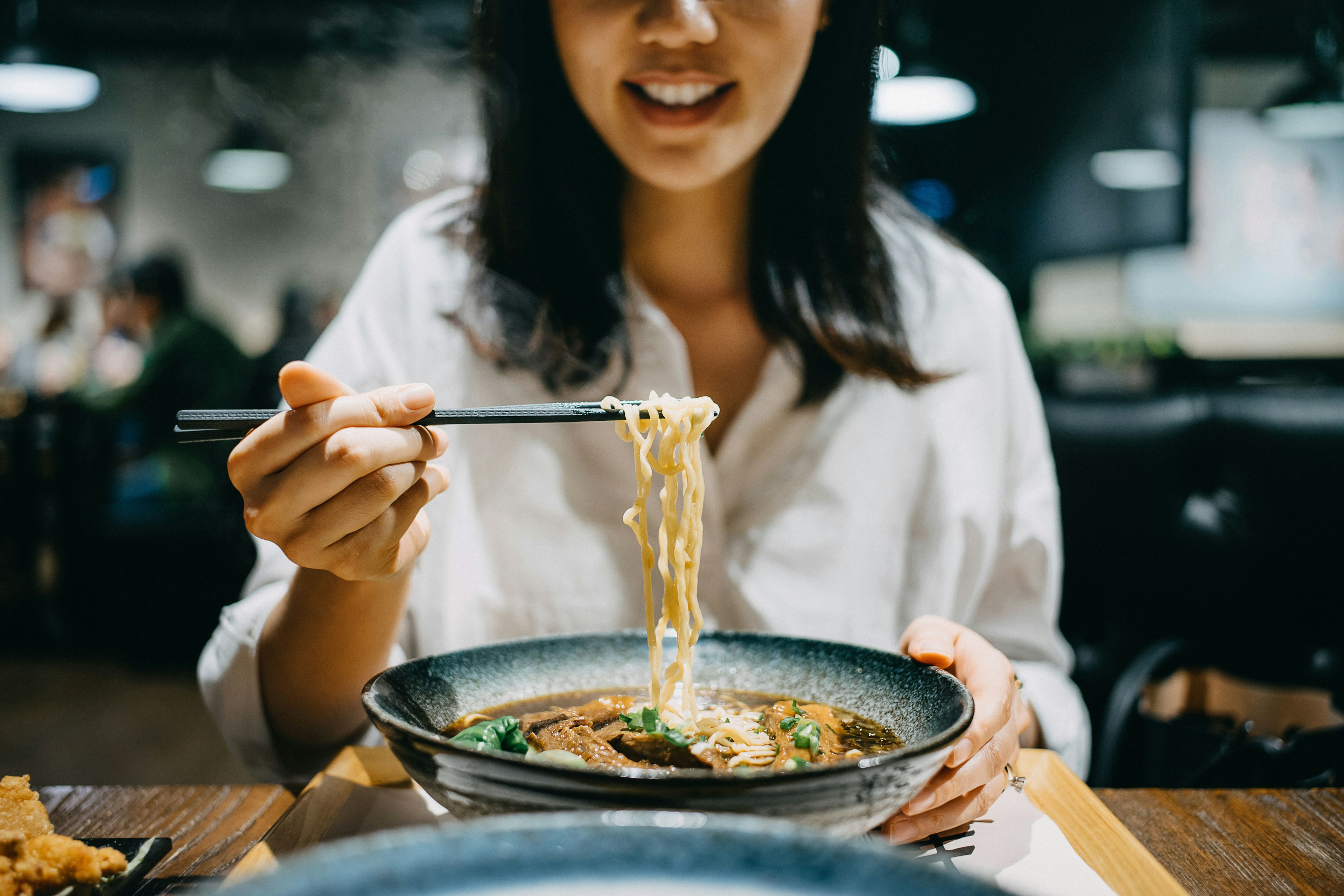 Smiling young woman enjoying soup noodles with side dishes at a restaurant