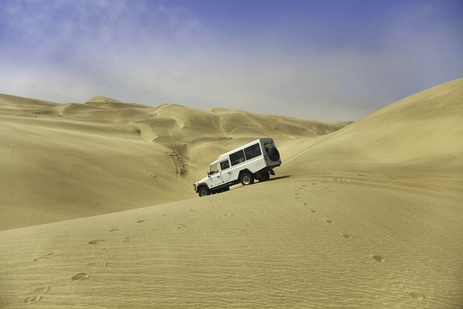 A white four wheel drive vehicle descends the sand dunes between Walvis bay and Sandwich harbour, Skeleton Coast, Namibia