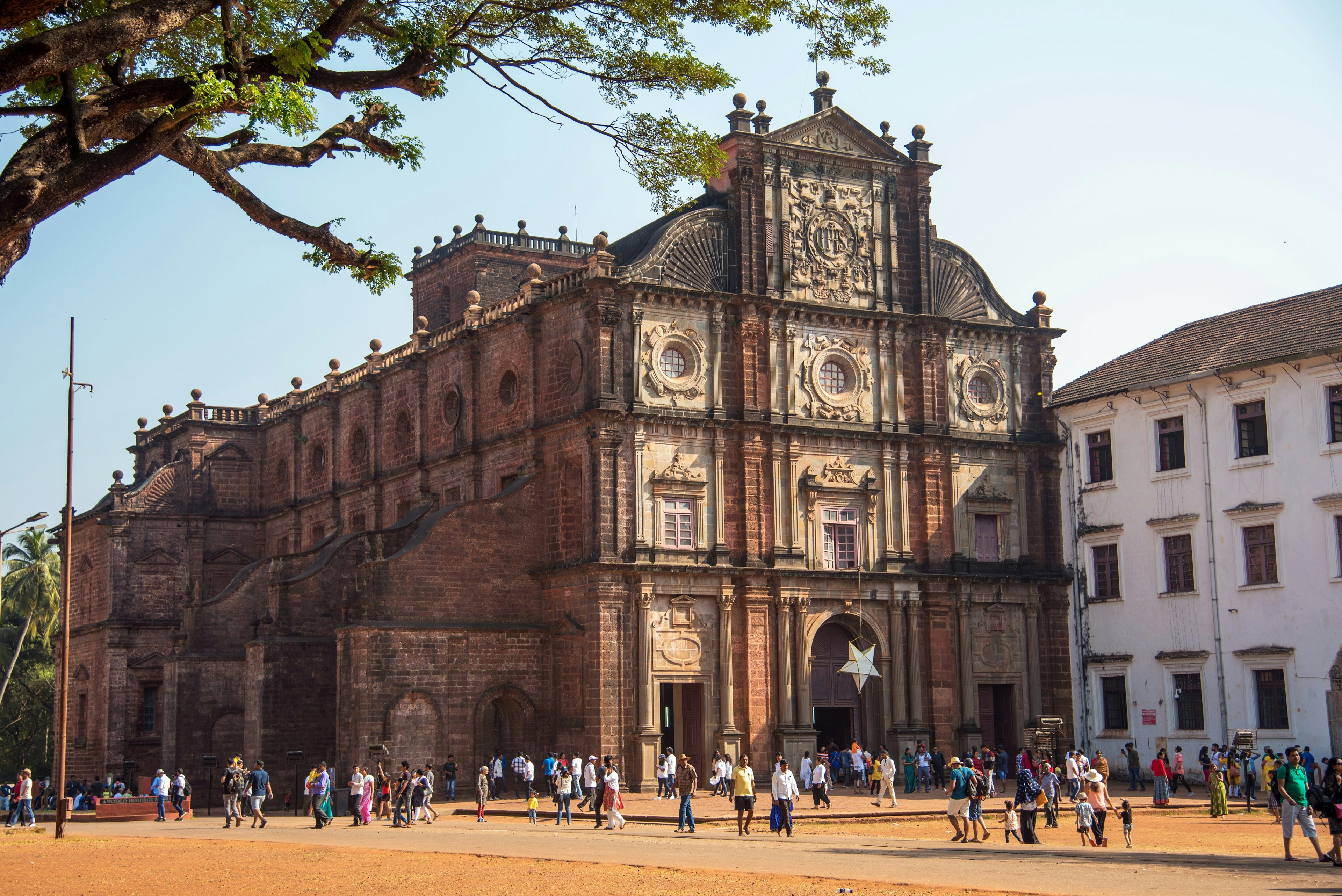 An imposing Portuguese church located in Old Goa, looming over the surrounding palm trees and scattering of people walking around the grounds.