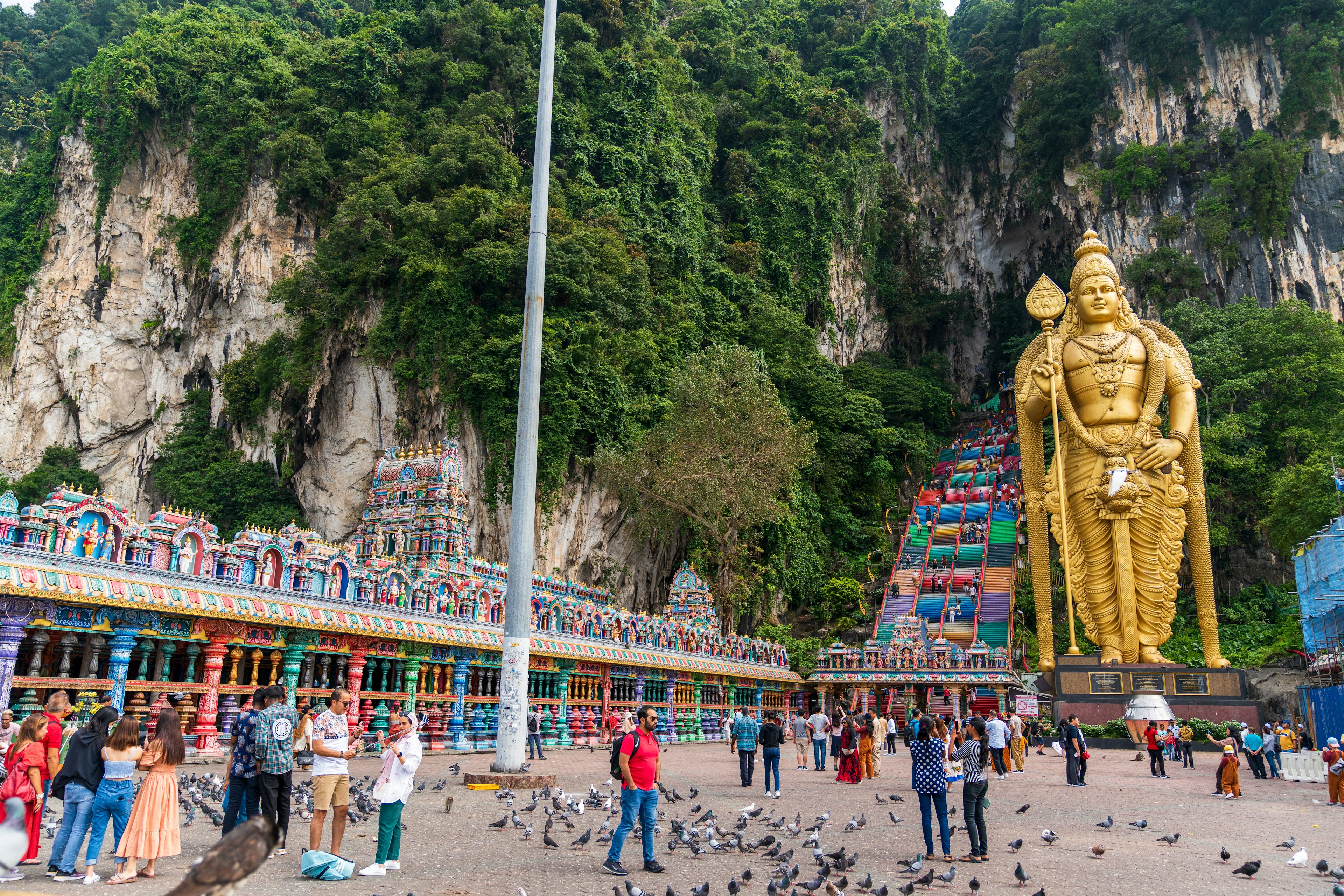 A huge gold statue stands in front of a rainbow-colored staircase leading up into a cave system in the rocks