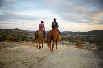 Two wranglers on horseback overlooking the Dixie Dude Ranch in Bandera, Texas.