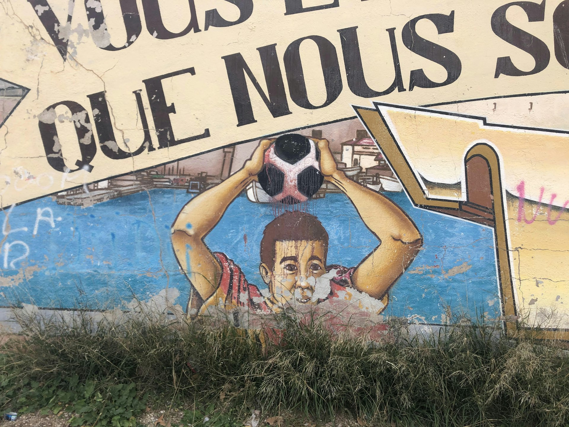 A mural showing a boy throwing in a soccer ball under the words "que nous" 