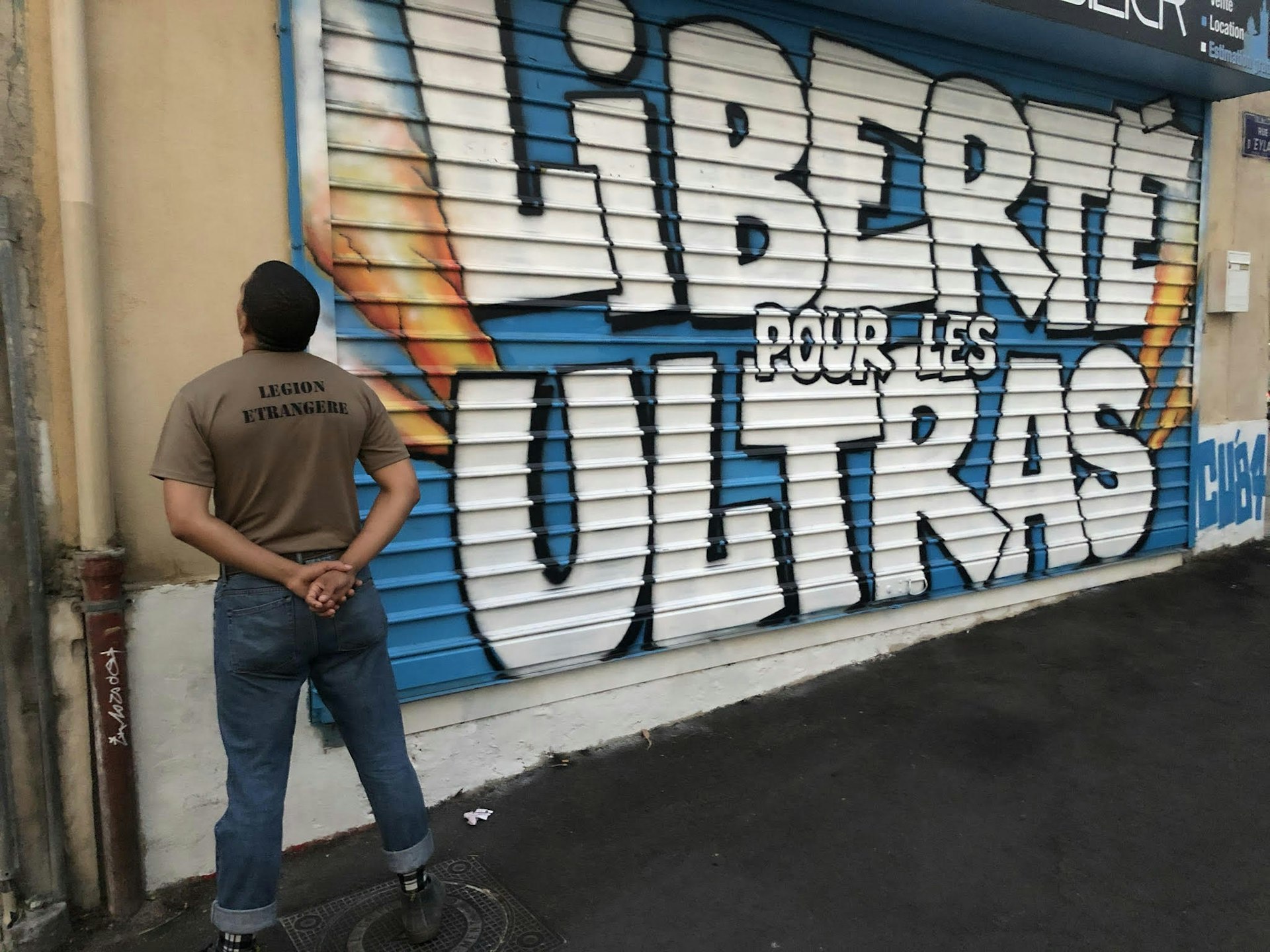 A man standing with his back turned, looking at graffiti that says "Liberté pour les Ultras"