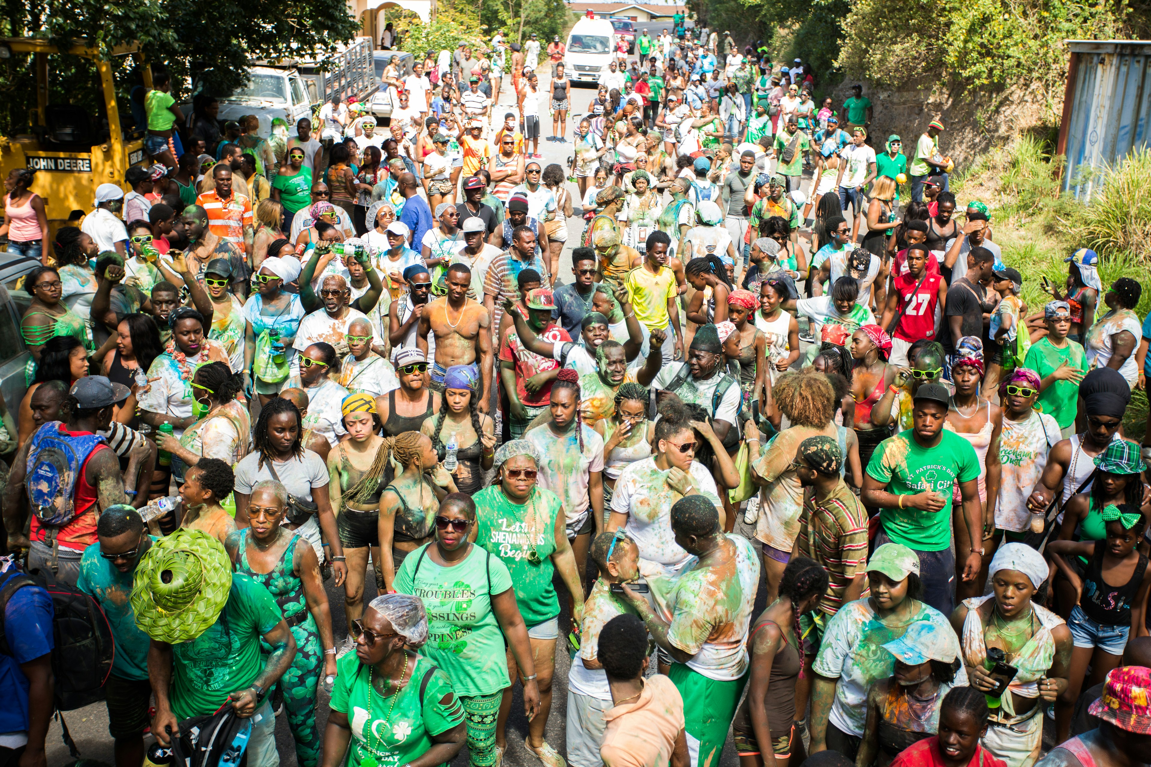 A crowd of people covered in colorful paint powder make their way down a street in a procession