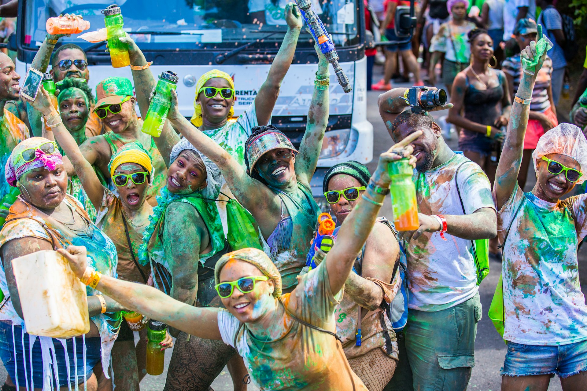 A crowd of people covered in paint, wearing sunglasses and carrying water bottles wave at the camera during a St Patrick's celebration in Montserrat