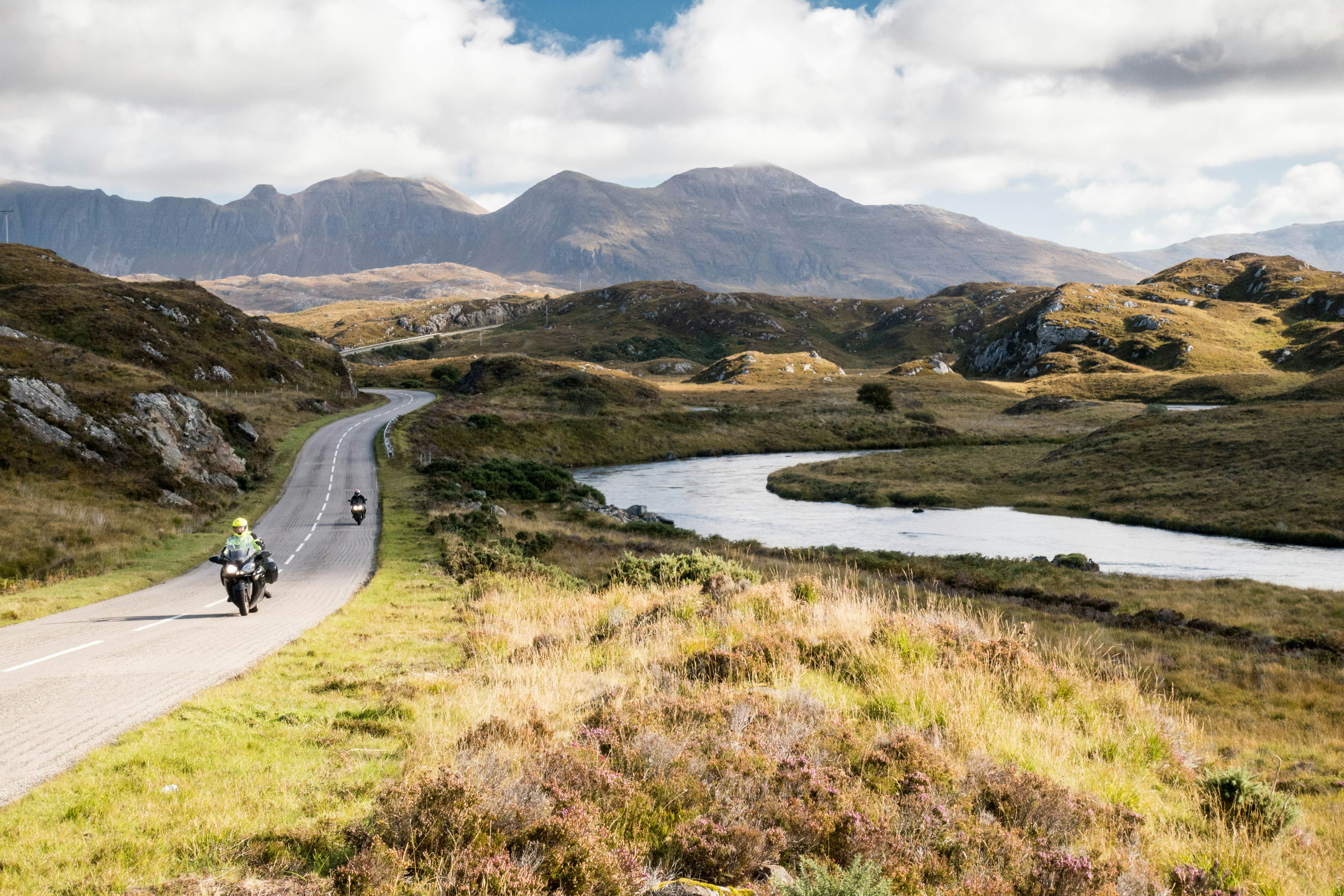 Motorcyclists drive down a road through the lush Scottish Highlands.