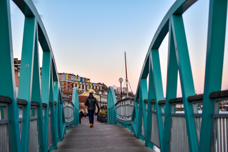 Man walking on Blue / Turquoise footbridge leading from Bristol Harbor towards the well known colorful houses of Clifton -Image; Shutterstock ID 1330383716; your: Sloane Tucker; gl: 65050; netsuite: Online Editorial; full: Destination Page
1330383716