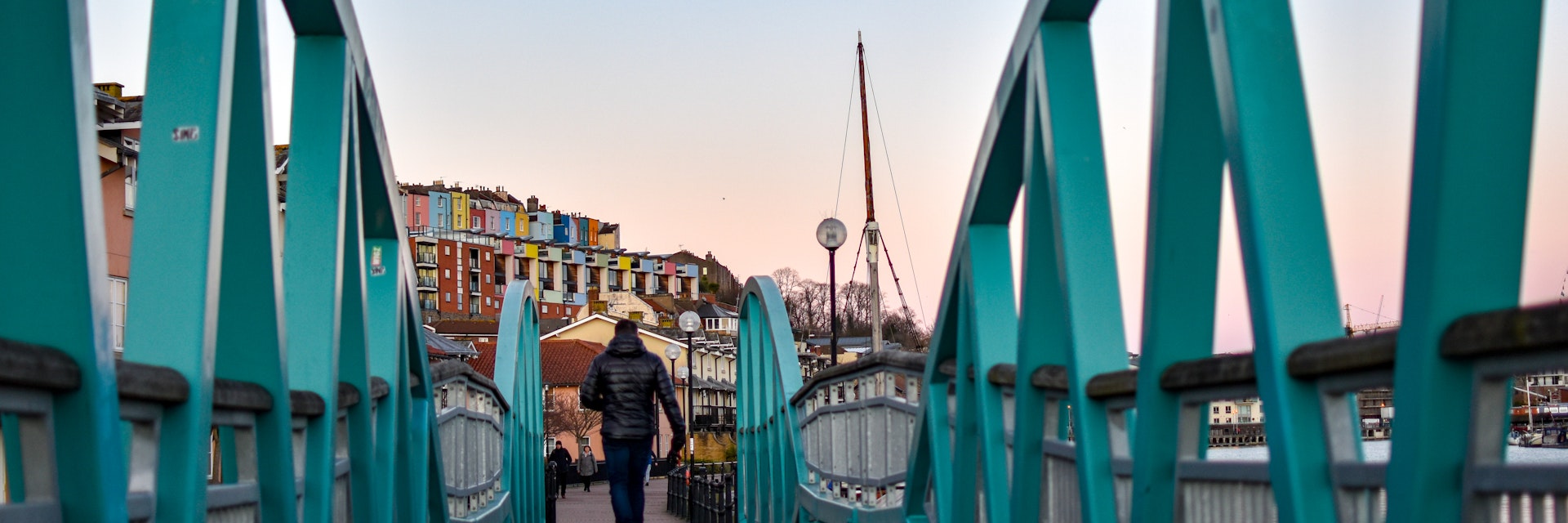 Man walking on Blue / Turquoise footbridge leading from Bristol Harbor towards the well known colorful houses of Clifton -Image; Shutterstock ID 1330383716; your: Sloane Tucker; gl: 65050; netsuite: Online Editorial; full: Destination Page
1330383716