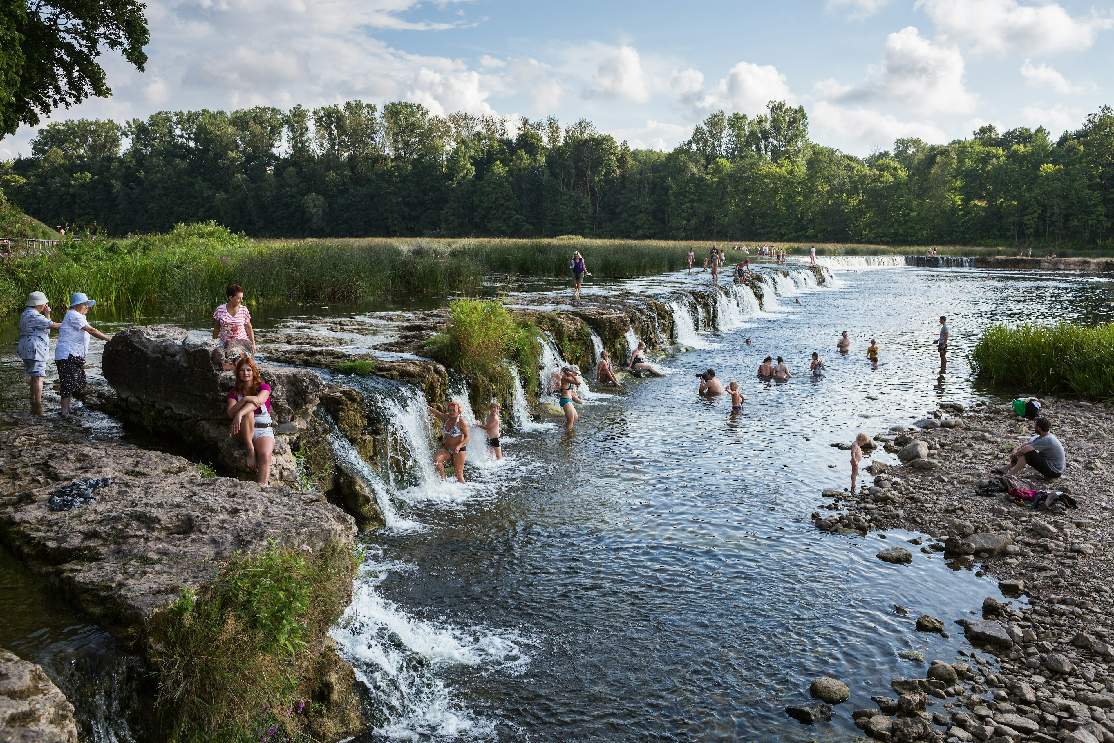 People are swimming by the Kuldiga waterfall.