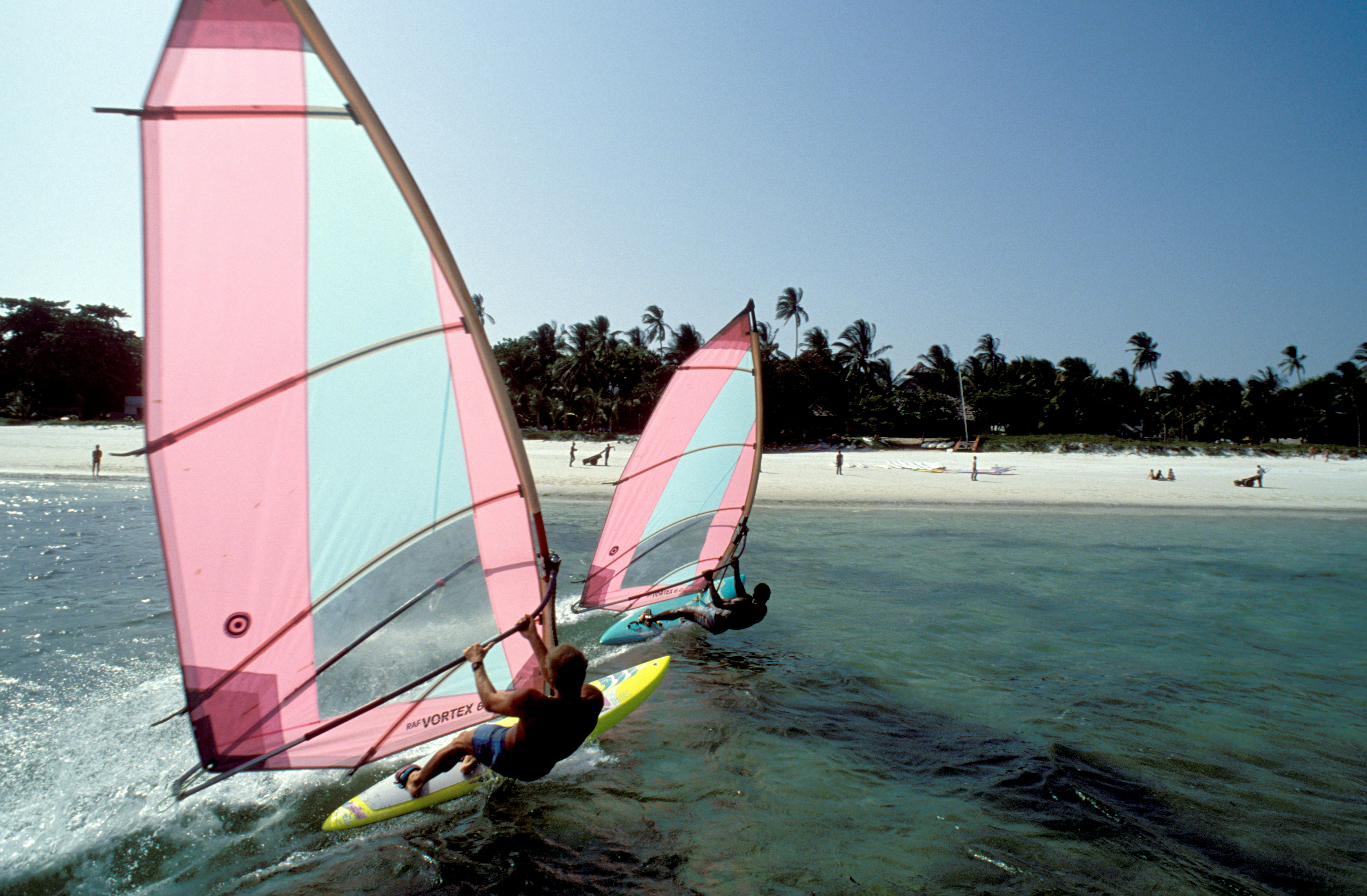 Two windsurfers just offshore from a lovely sandy beach.