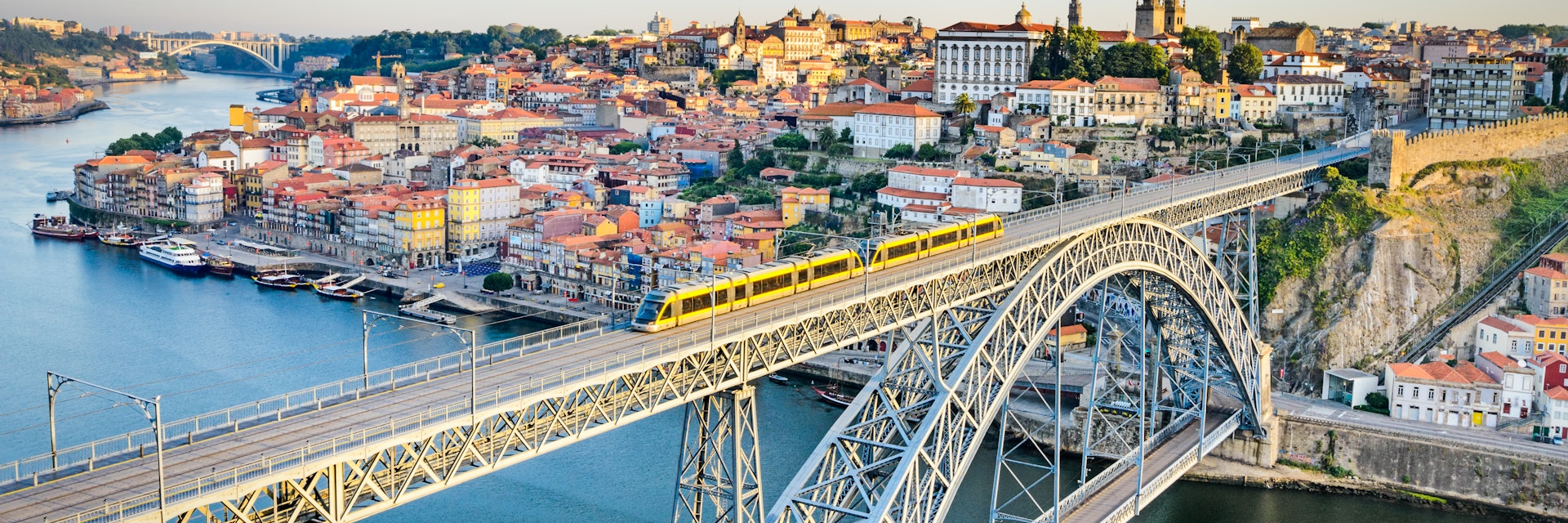 A metro train crosses the Dom Luiz bridge with the historic city of Porto beyond.
