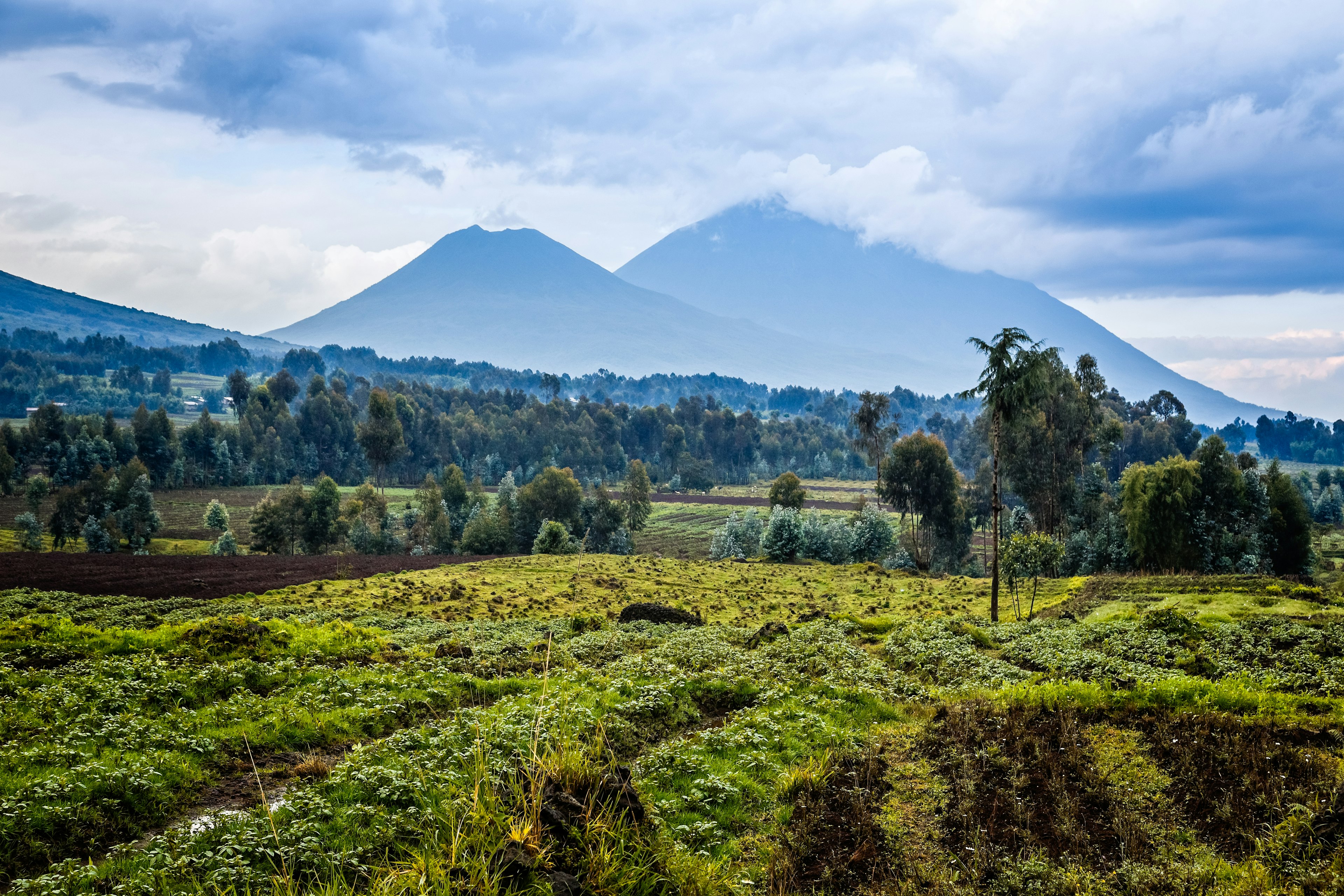 A cloud-topped volcano surrounded by green farmland and fields