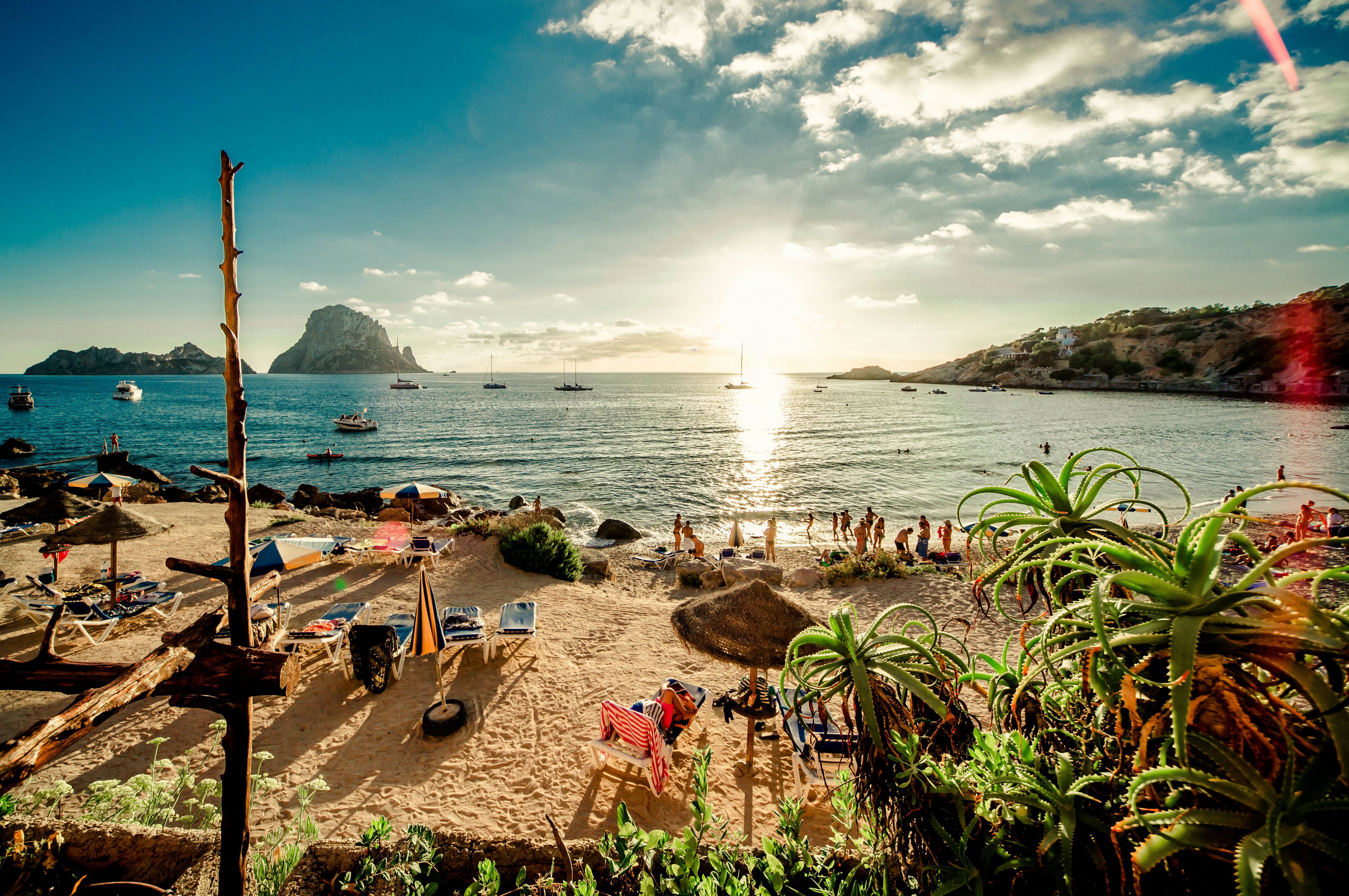 Sunbathers frollick by the sea at sunset on a sandy beach in Ibiza.