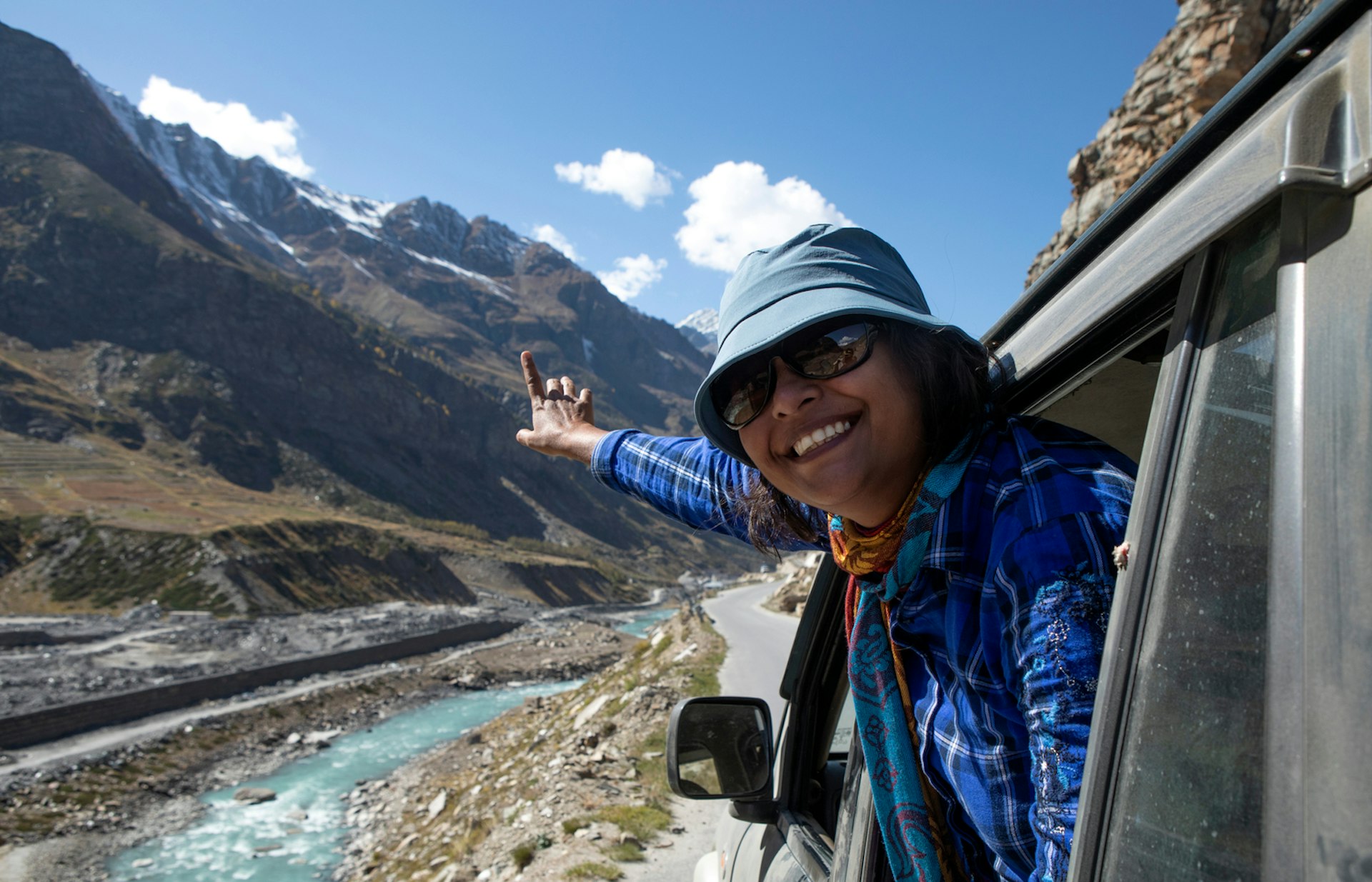 A woman smiles as she leans out the window of a vehicle and points to a blue river running alongside the road