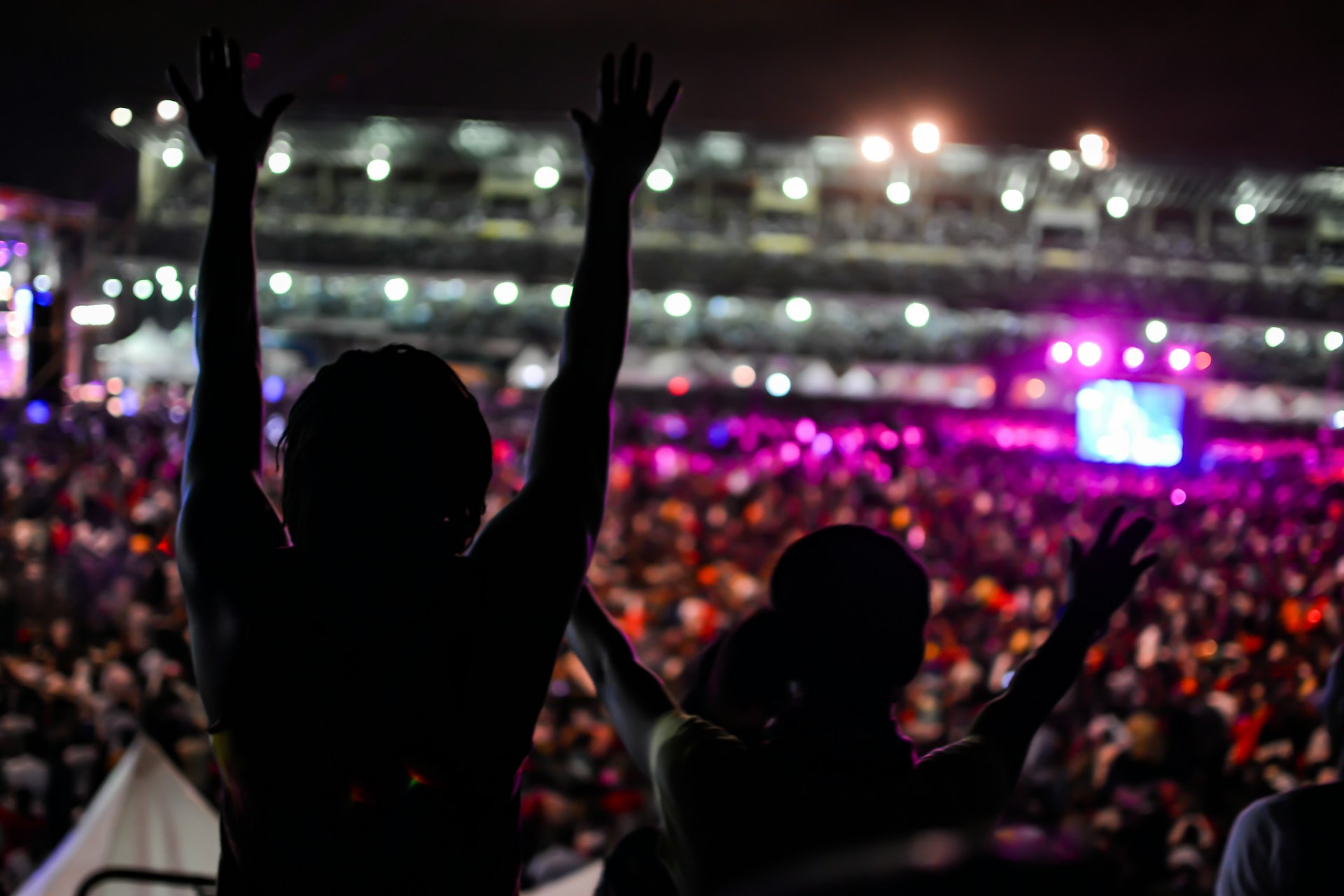 People in silhouette with their hands in the air at a concert arena