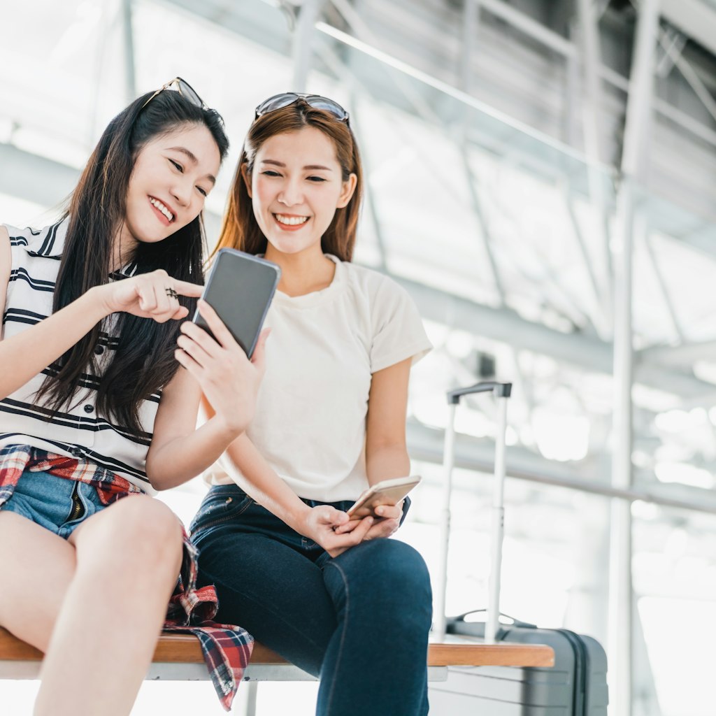 Two happy Asian girls using smartphone checking flight or online check-in at airport together, with luggage. Air travel, summer holiday, or mobile phone application technology concept; Shutterstock ID 624203687; your: Ben N Buckner; gl: 65050; netsuite: Online Editorial; full: Ben Buckner - Chase Southwest
624203687