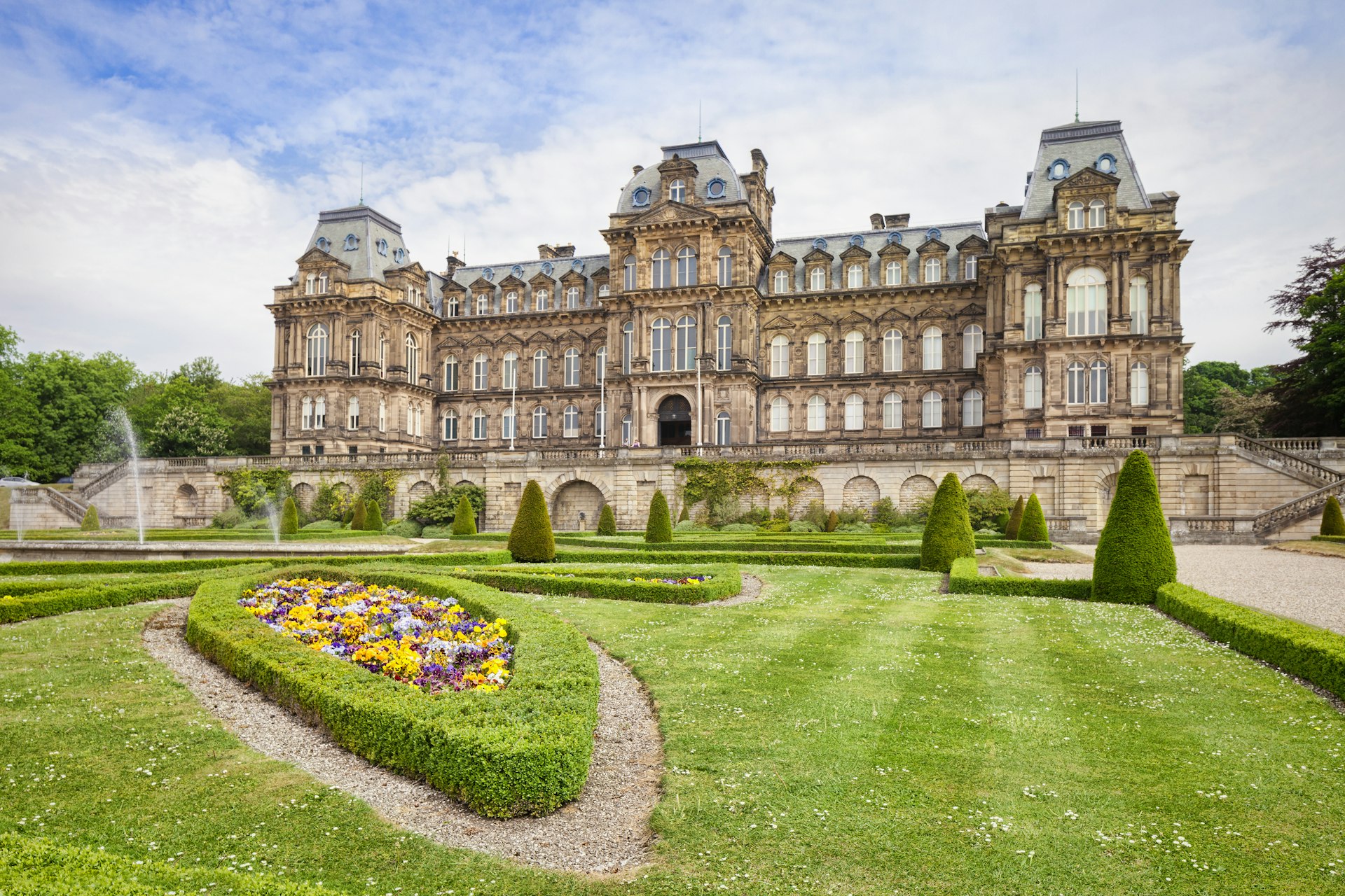 The exterior of a grand palatial building with manicured lawns and pretty flowerbeds
