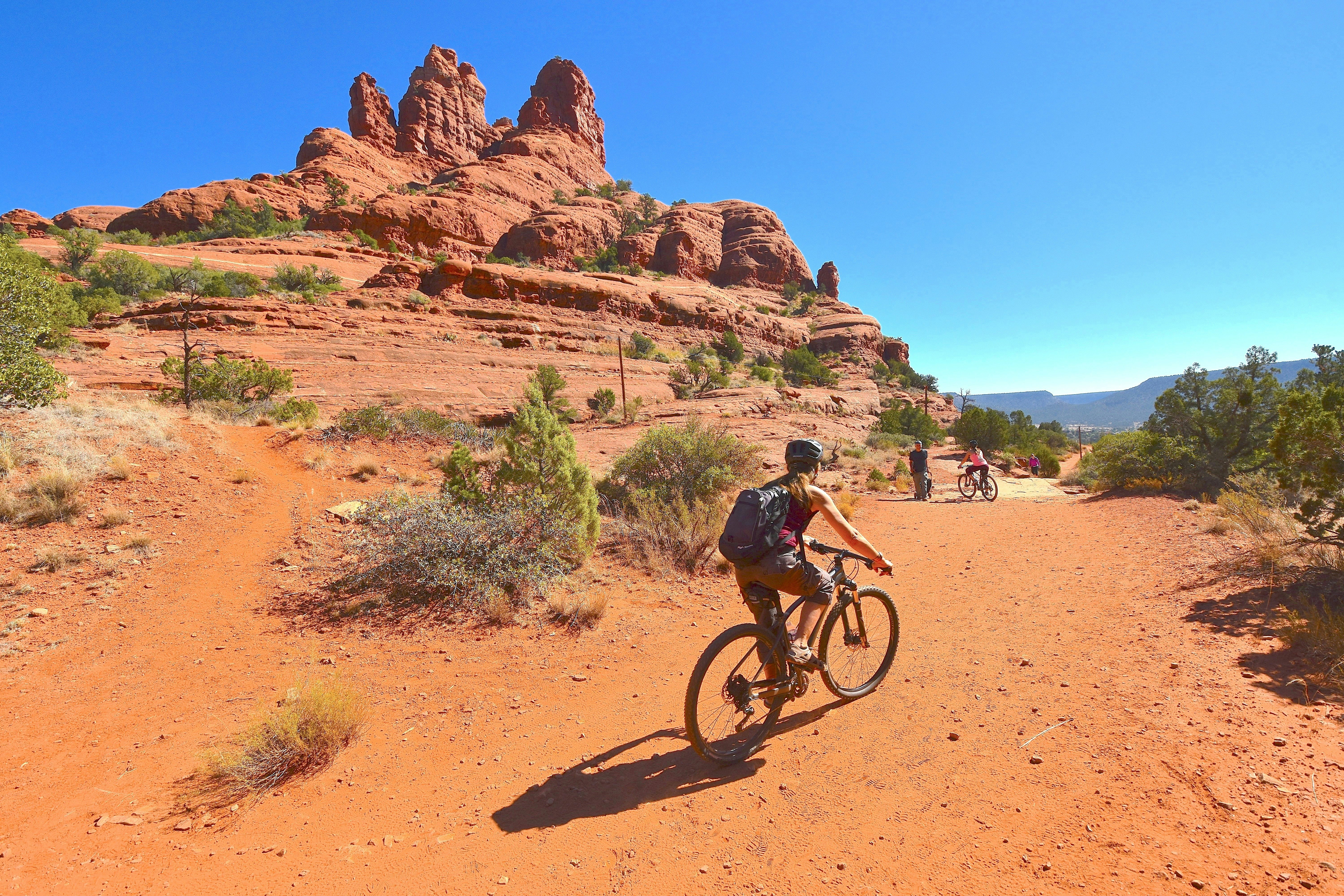A biker pedals over a red-sand track in a desert landscape.