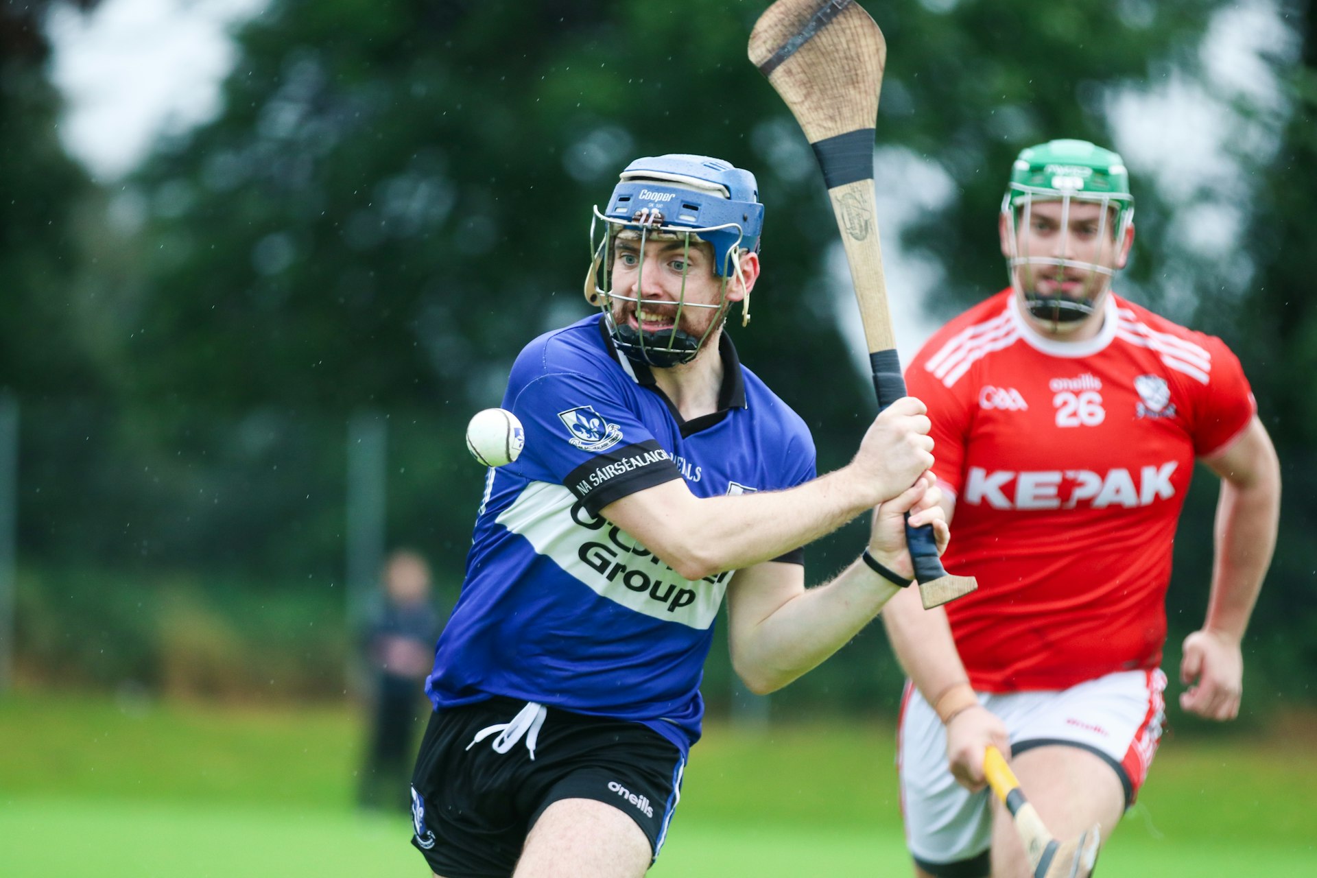 A helmeted hurling player in blue grimaces as he prepares to whack the sliotar