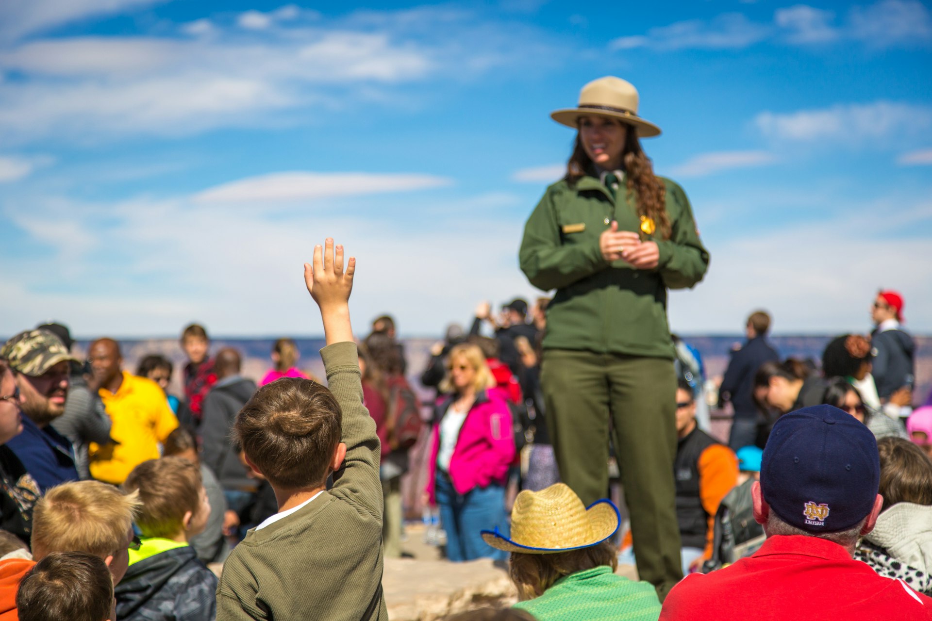 A kid with his hand raised and a park ranger replying to his question at the south rim of Grand Canyon National Park, Arizona