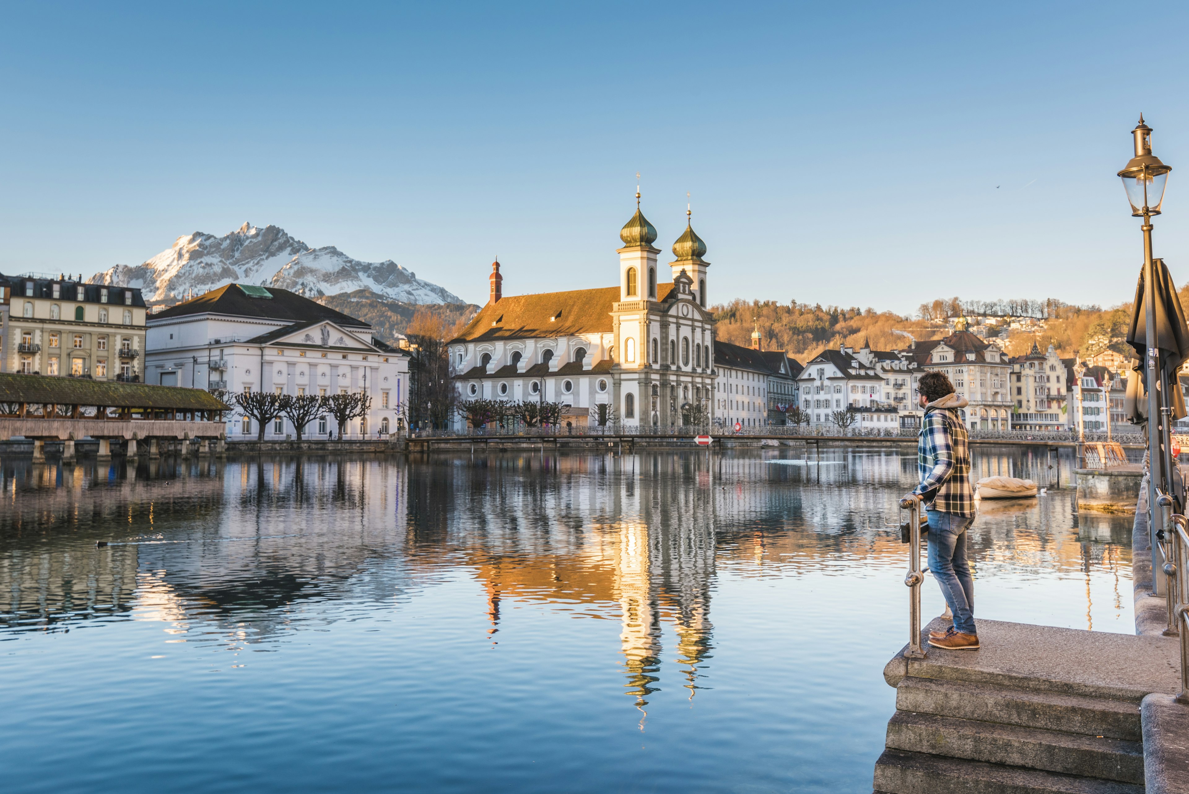 A man looks at the Jesuit Church and Mount Pilatus from the banks of Reuss River in Lucerne, Switzerland