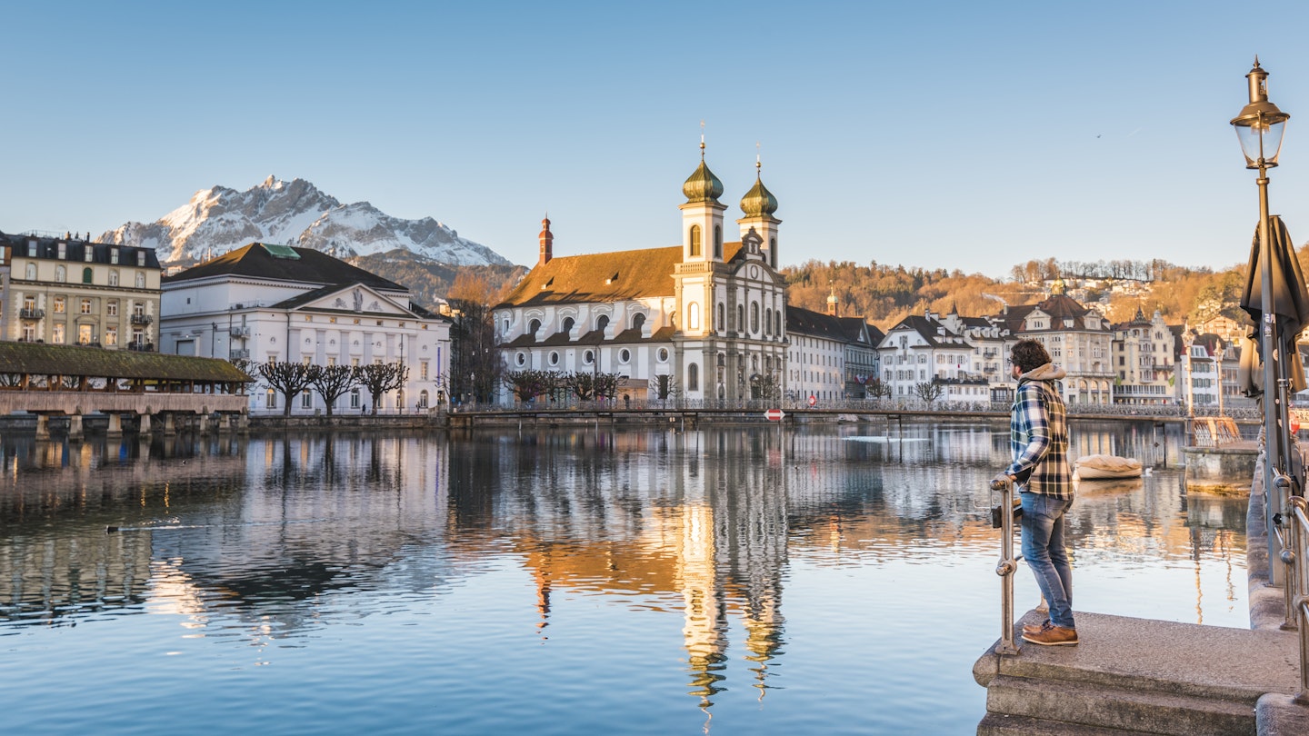 One man looking at the Jesuit Church and Mount Pilatus from the banks of Reuss river in Lucerne, Switzerland