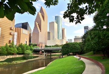 Wide shot of Houston's modern skyline and paved bicycle/walking path in Buffalo Bayou Park on a summer afternoon