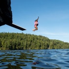 Small girl with a life jacket on, jumps off a diving board into a remote lake in Michigan's Upper Peninsula while  her brother watches.
1177965797
A small girl with a life jacket on jumps off a diving board into a remote lake in Michigan's Upper Peninsula while her brother watches.