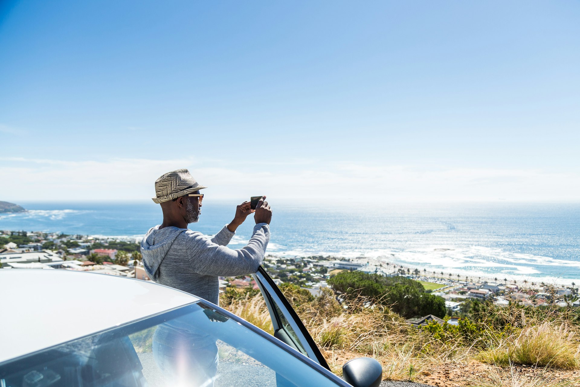 A tourist stands by his car taking a photograph of the coastline near Cape Town