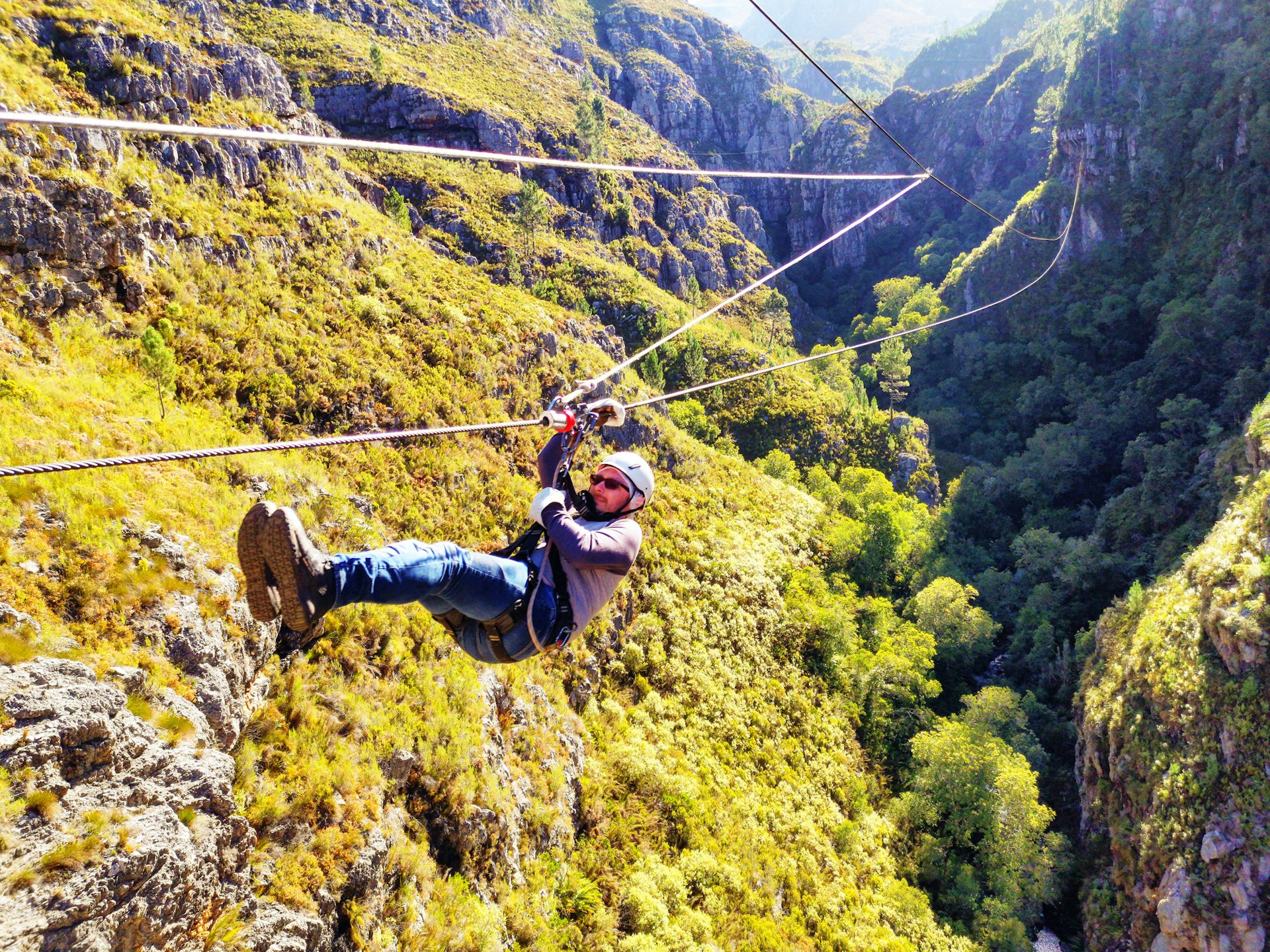 A man in safety gear slides along a zipline through a canyon