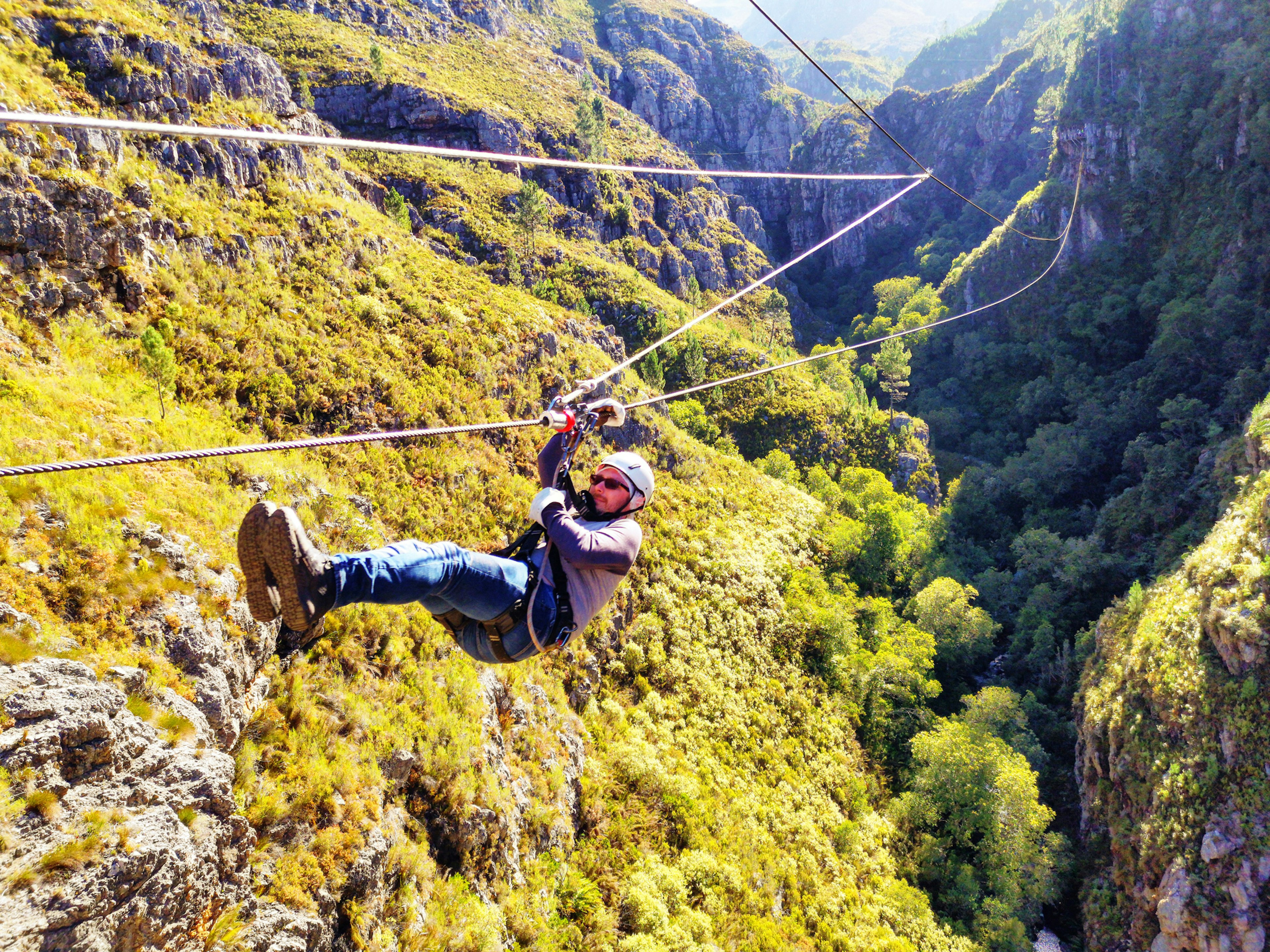 A man in safety gear slides along a zipline through a canyon