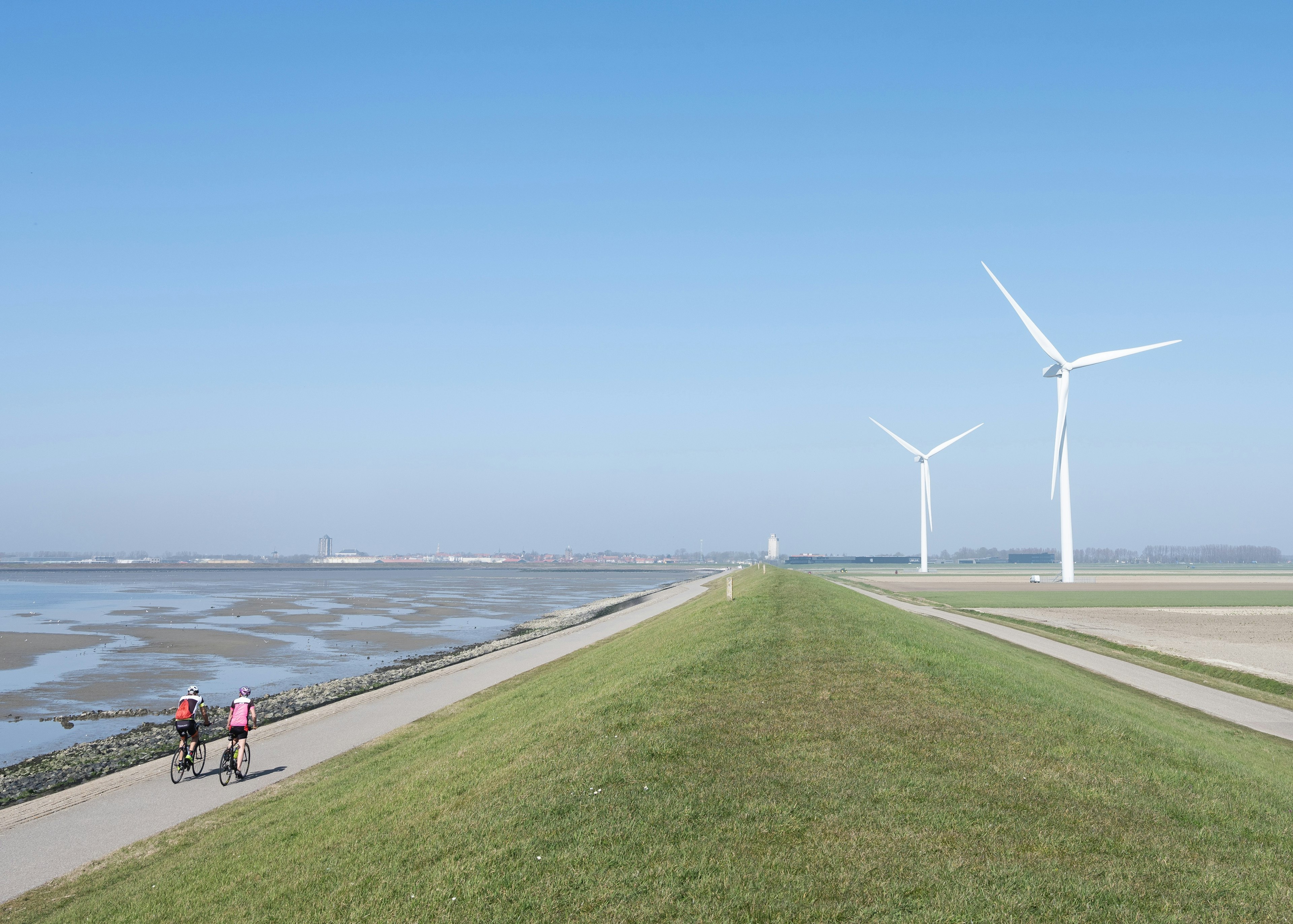 Two men cycle on a bike path by water and wind turbines, Schouwen-Duiveland, Zeeland, the Netherlands