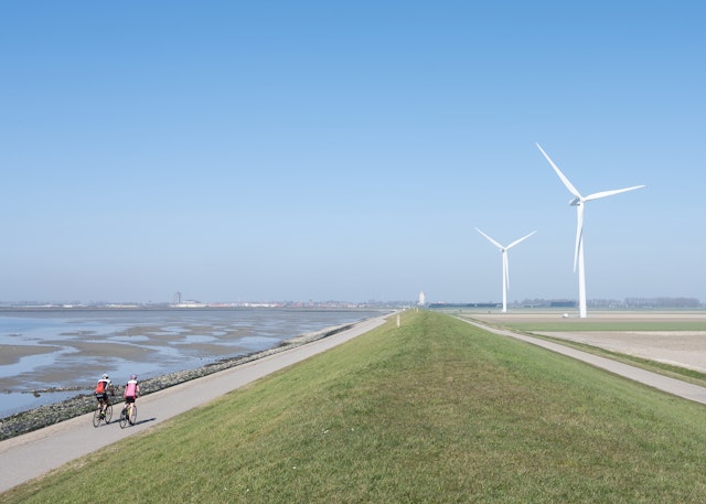 Two men cycle on a bike path by water and wind turbines, Schouwen-Duiveland, Zeeland, the Netherlands