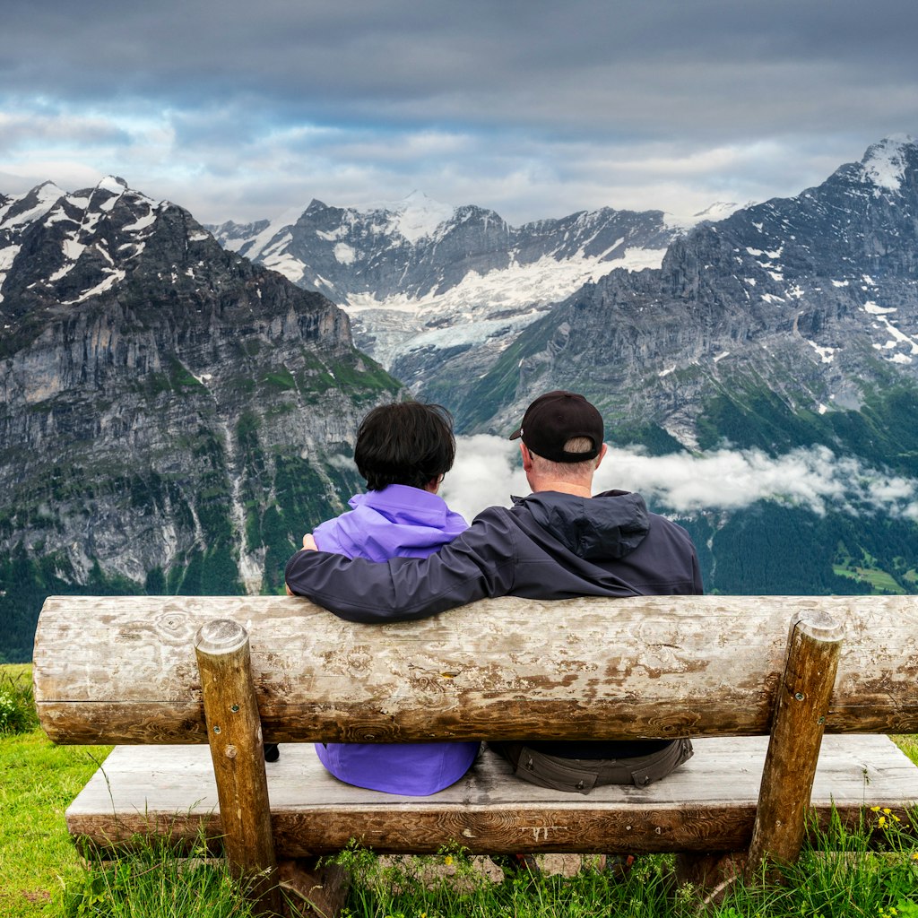 Senior couple sitting on wood bench enjoying the view at the top of First (pronounced Feerst)  mountain in Grindelwald, Switzerland.
1453171193