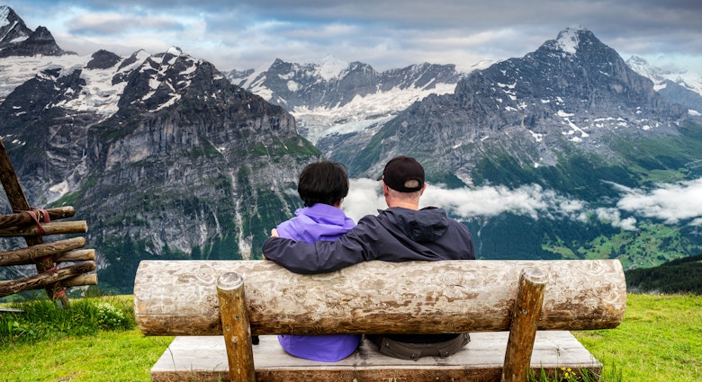 Senior couple sitting on wood bench enjoying the view at the top of First (pronounced Feerst)  mountain in Grindelwald, Switzerland.
1453171193
