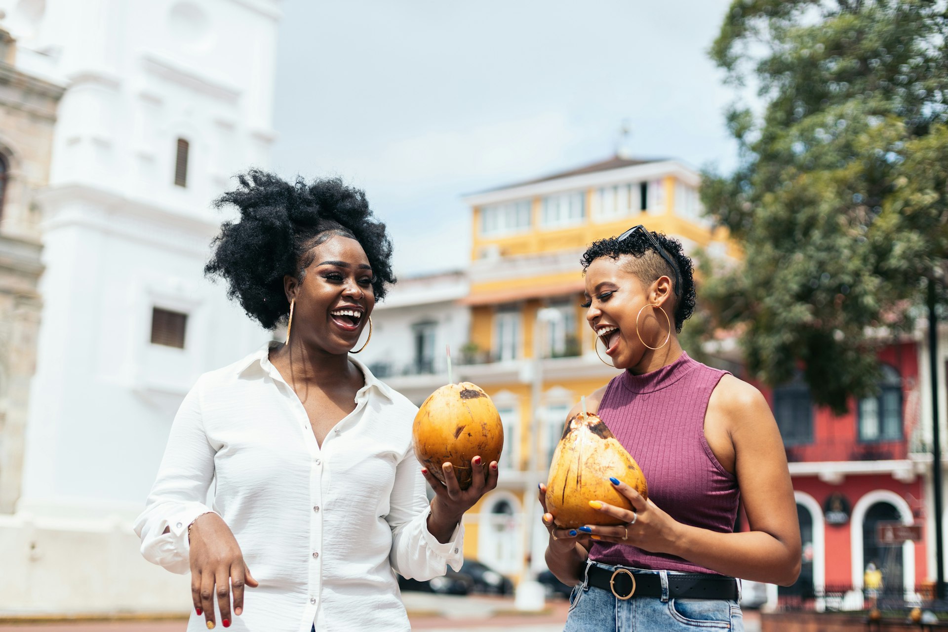 Latin American women stylish friends having fun walking on the street of Panama City drinking coconuts