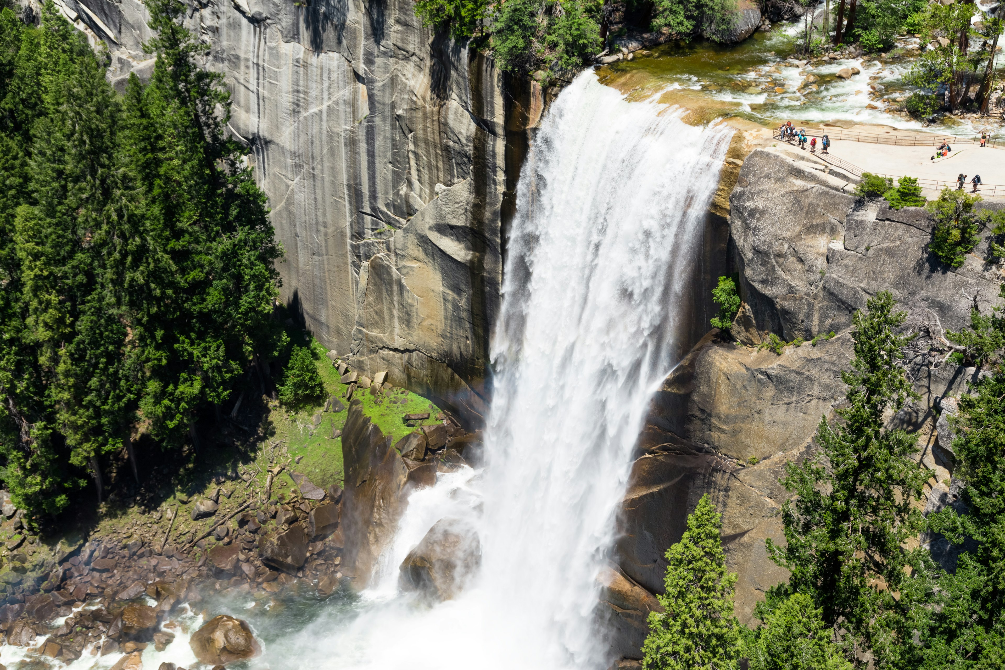 A waterfall in heavy flow cascades down into a pool. People watch from a viewing platform