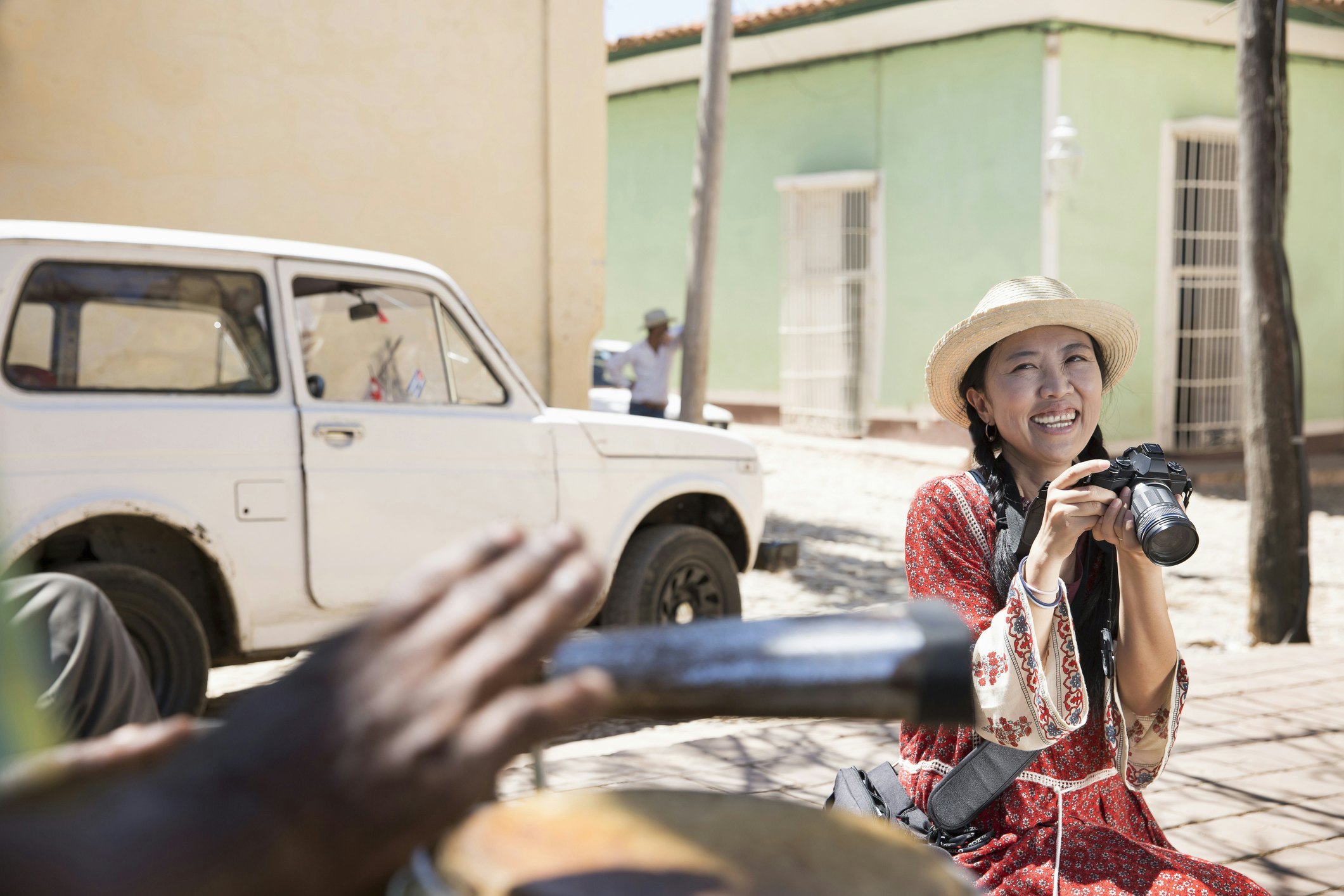 A woman holding a camera smiles with an old-fashioned car in the background