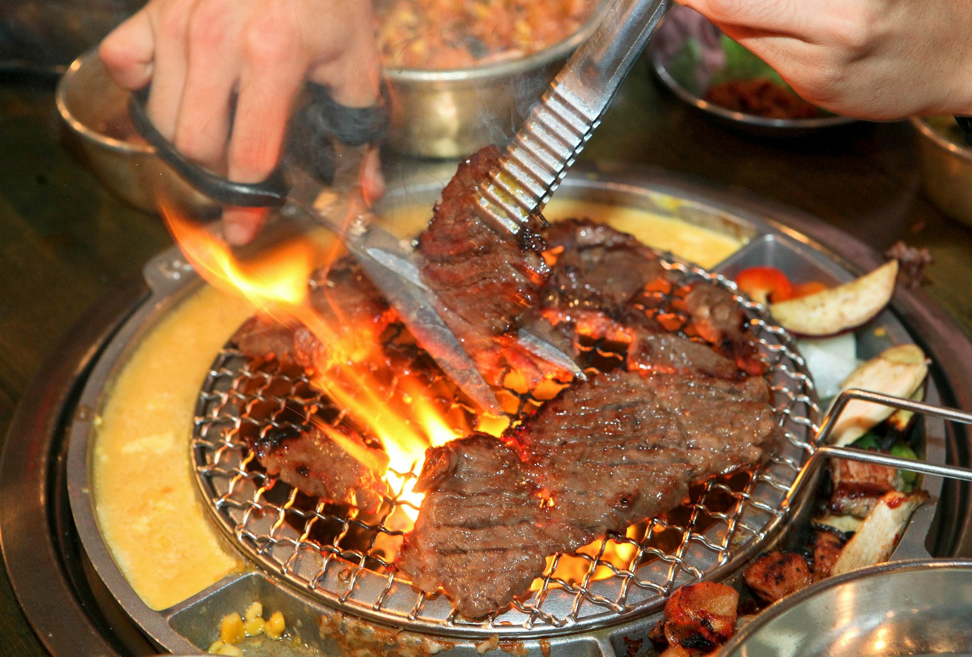 A patron cuts galbi beef into smaller pieces as it cooks on a burner at his table at a Korean BBQ restaurant