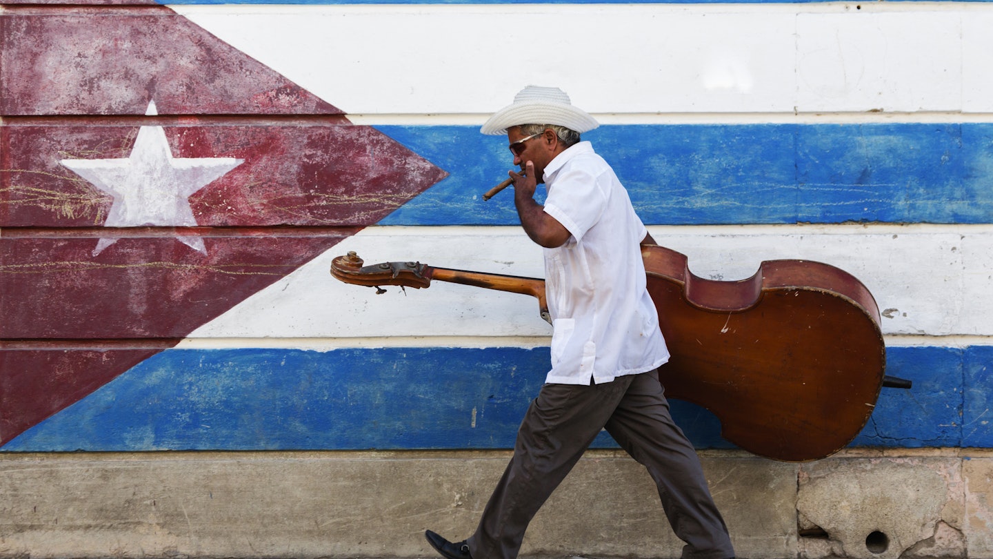 573064785
50-54 years, bass, carrying, cello, cigar, color image, Cuba, cuban flag, day, flag, full length, hat, horizontal, latin american and hispanic ethnicity, lifestyle, looking down, man, mature adult, mature men, motion, mural, music, musician, one person, outdoors, patriotism, people, photography, Santiago, Santiago de Cuba, side view, sidewalk, smoking, striped, sunglasses, travel, travel destinations, upright bass, urban, walking