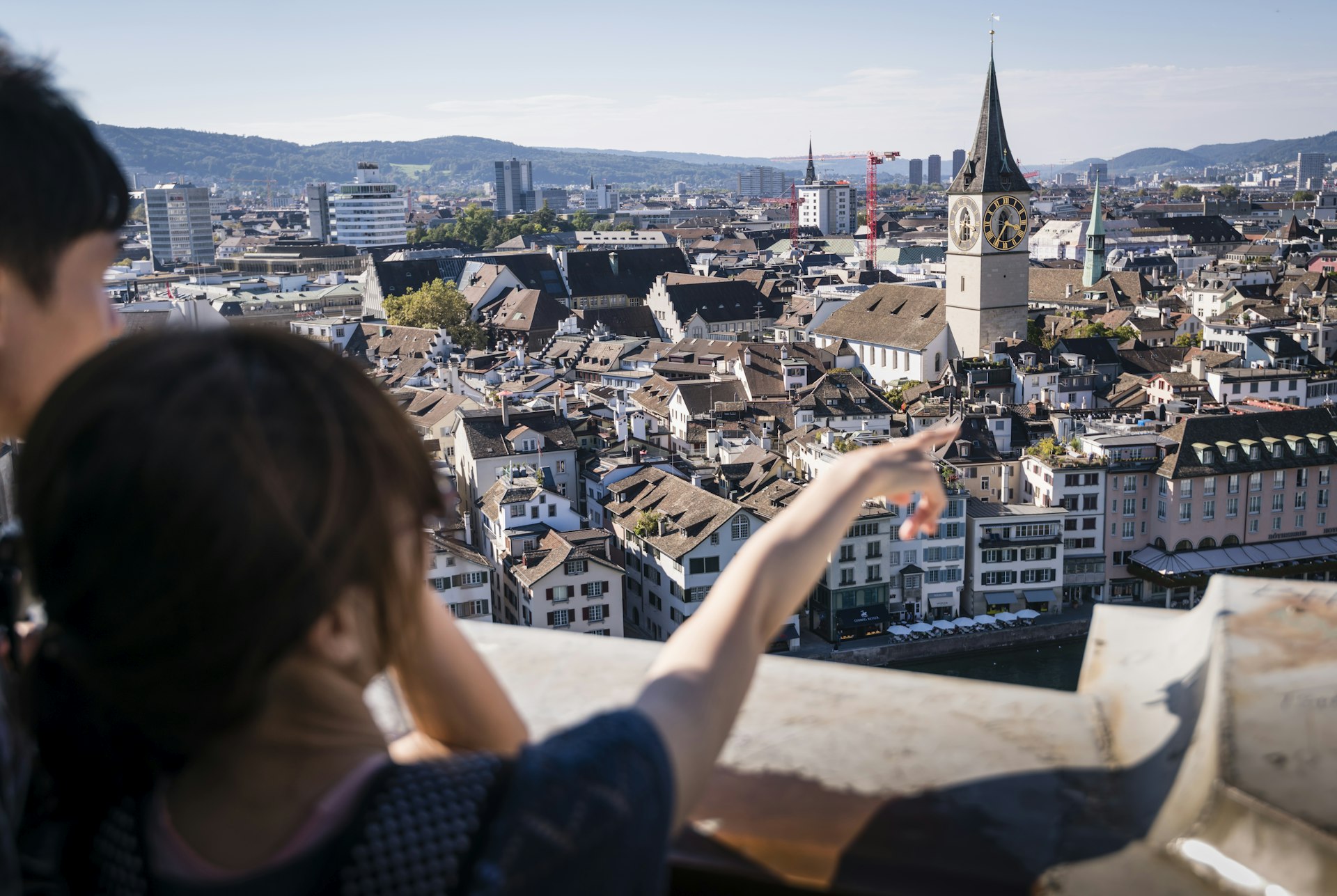 Two tourists are taking a look at Zurich's old town from the observation deck on top of Grossmunster cathedral