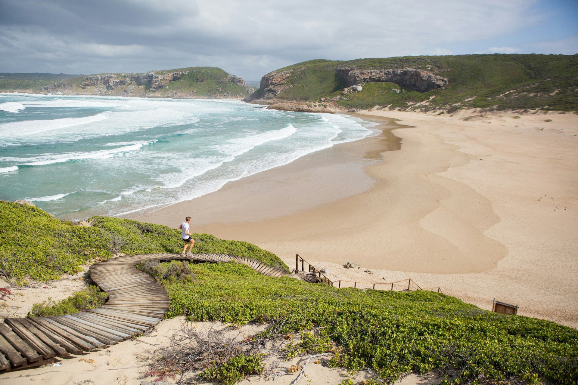 Woman running along a wooden boardwalk towards the ocean and an empty beach