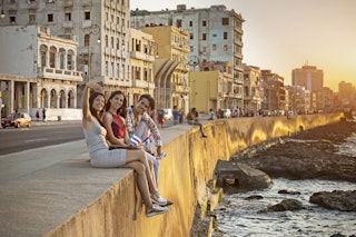 Young friends taking selfie while sitting on retaining wall in Havana. Male and females are relaxing in Malecon during sunset. They are enjoying vacation.
801149840
старая гавана, creativecontentbrief
Young friends take selfies while sitting on a wall along the Malecon in Havana as the sun sets.